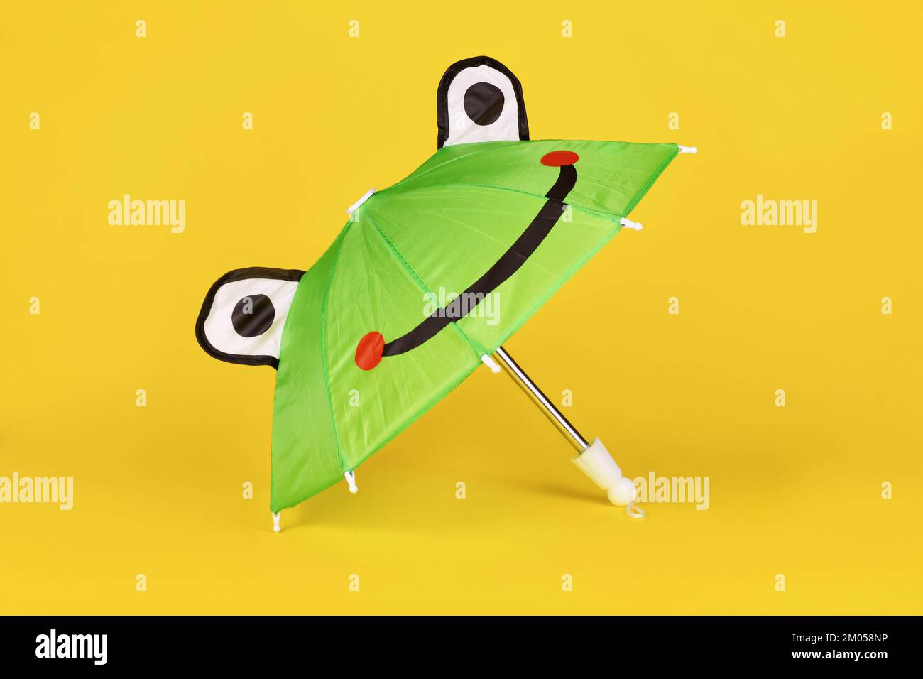 Süßer grüner Regenschirm mit Froschgesicht auf gelbem Hintergrund Stockfoto