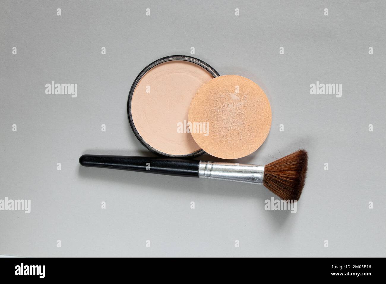 Pulver in einem runden Kunststoffpaket und eine Bürste auf grauem Hintergrund, Nahaufnahme von Frauenkosmetik, Fundamentpulver Stockfoto