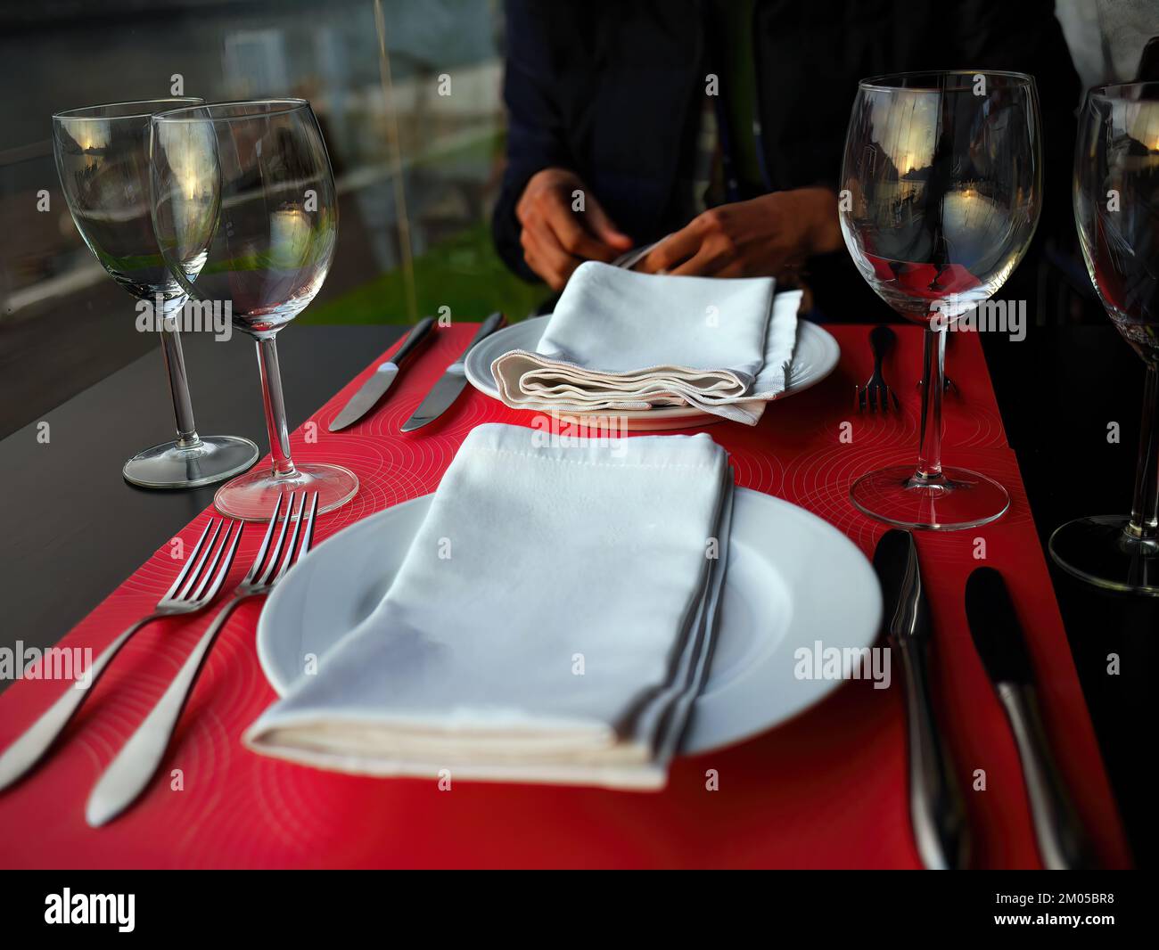 Eine Person in dunkelblauem Kleid, die auf dem Esstisch sitzt, einen Teil des Körpers, auf das Abendessen wartet, auf einem Holztisch mit Abendgarderobe serviert, Gaia, Porto, Portugal Stockfoto