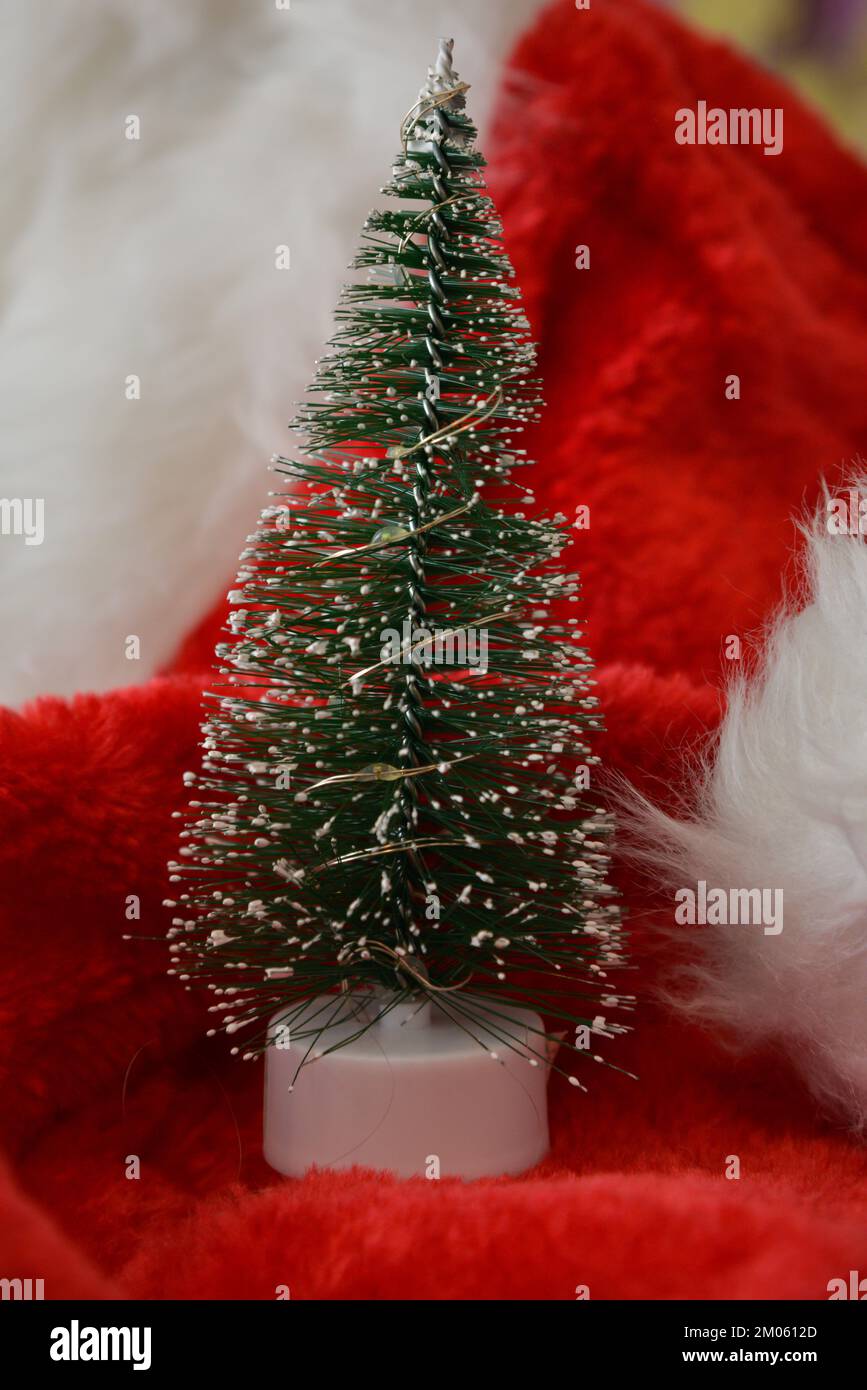 Weihnachtsdekorationen. Ein kleiner künstlicher Weihnachtsbaum mit künstlichem Schnee auf einem roten Weihnachtsmann-Hut. Stockfoto