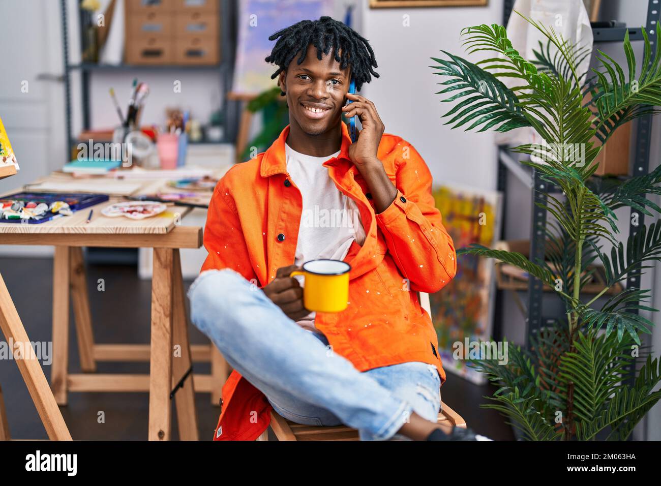 afroamerikanischer Künstler trinkt Kaffee-Talkking auf dem Smartphone im Kunststudio Stockfoto