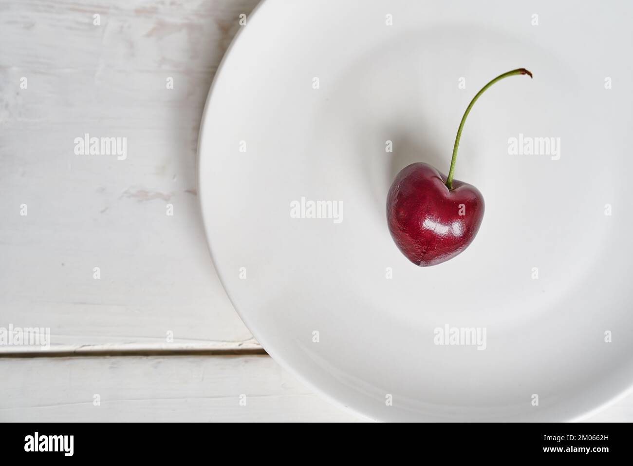 Eine herzförmige Kirsche auf einem weißen Teller. Reife, frische, saftige Beere auf weißem Hintergrund. Fruchthintergrund. valentinstag. Mit Platz zum Kopieren. Hochwertiges Foto Stockfoto