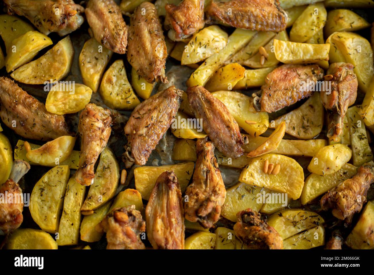 Traditionelle Bratkartoffeln und Hähnchenflügel im Ofen gewürzt mit Rosmarin und Pinienkernen Stockfoto