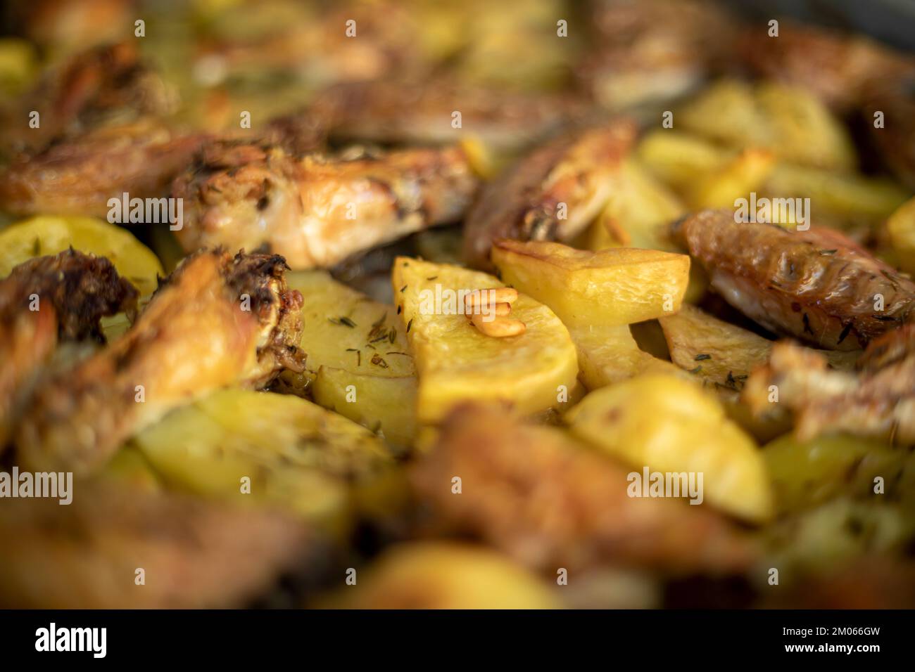 Traditionelle Bratkartoffeln und Hähnchenflügel im Ofen gewürzt mit Rosmarin und Pinienkernen Stockfoto