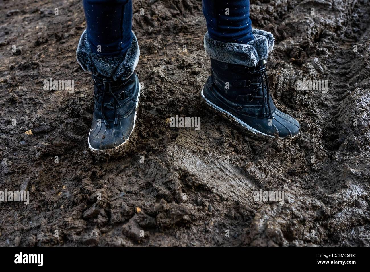 Kinderfüße in dreckigen, verschmutzten Stiefeln, schlammiger Hintergrund. Schmutzige warme Stiefel im Schlamm. Fotos in hoher Qualität Stockfoto