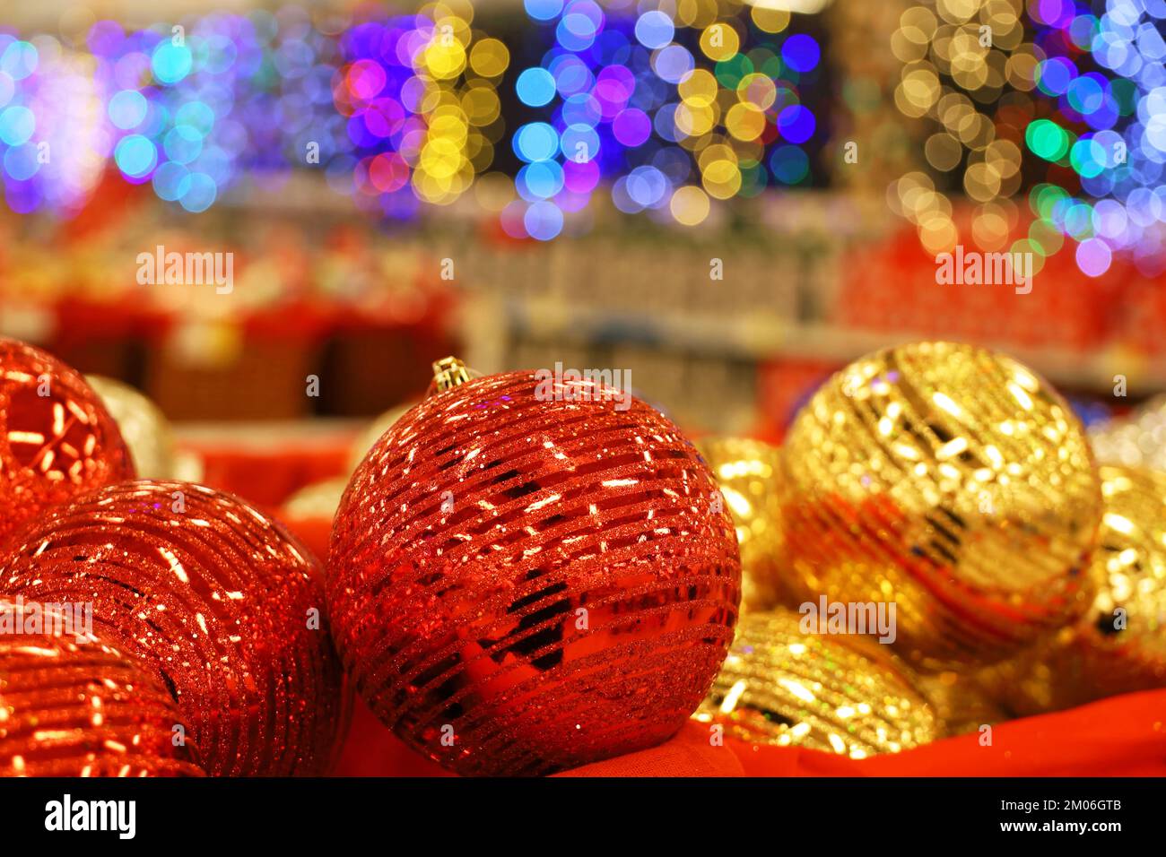 Weihnachtsspielzeug, rote und goldene Kugeln in rotem Korb auf verschwommenem festlichem Hintergrund. Neujahrsdekoration in einem Geschäft Stockfoto