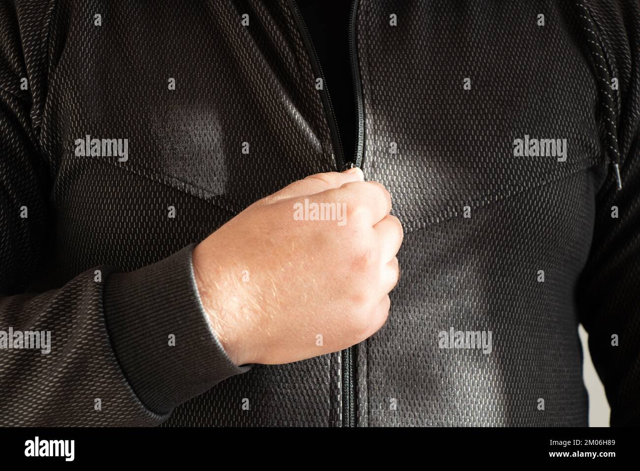 Männliche Hand öffnet den Reißverschluss an einer grauen Sportjacke, Jacke mit Reißverschluss und Schloss Stockfoto