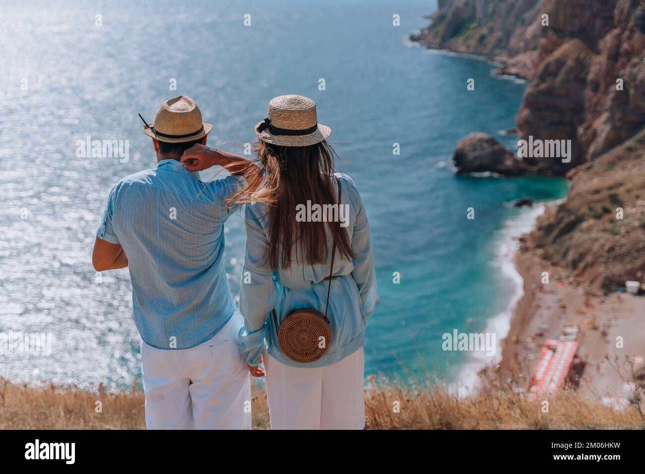Das Paar steht mit dem Rücken zum Publikum und schaut hinunter auf die wunderschöne Meereslandschaft. Sie tragen Hüte, blaue Hemden und weiße Shorts. Stockfoto
