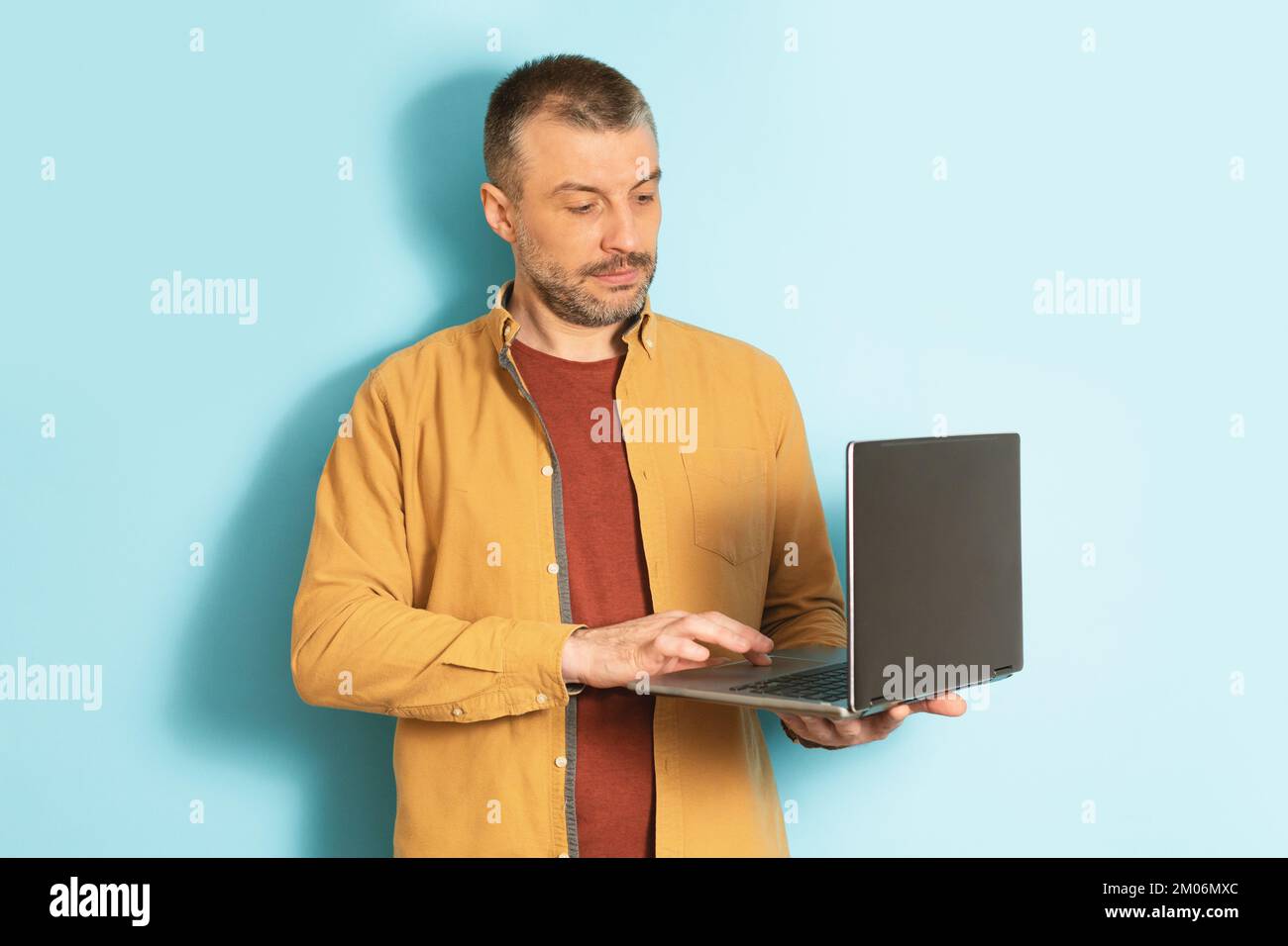 Kluger Geschäftsmann, Mitarbeiter, der am Computer arbeitet. Ein reifer Mann tippt auf einem Laptop, der auf blauem Hintergrund steht Stockfoto