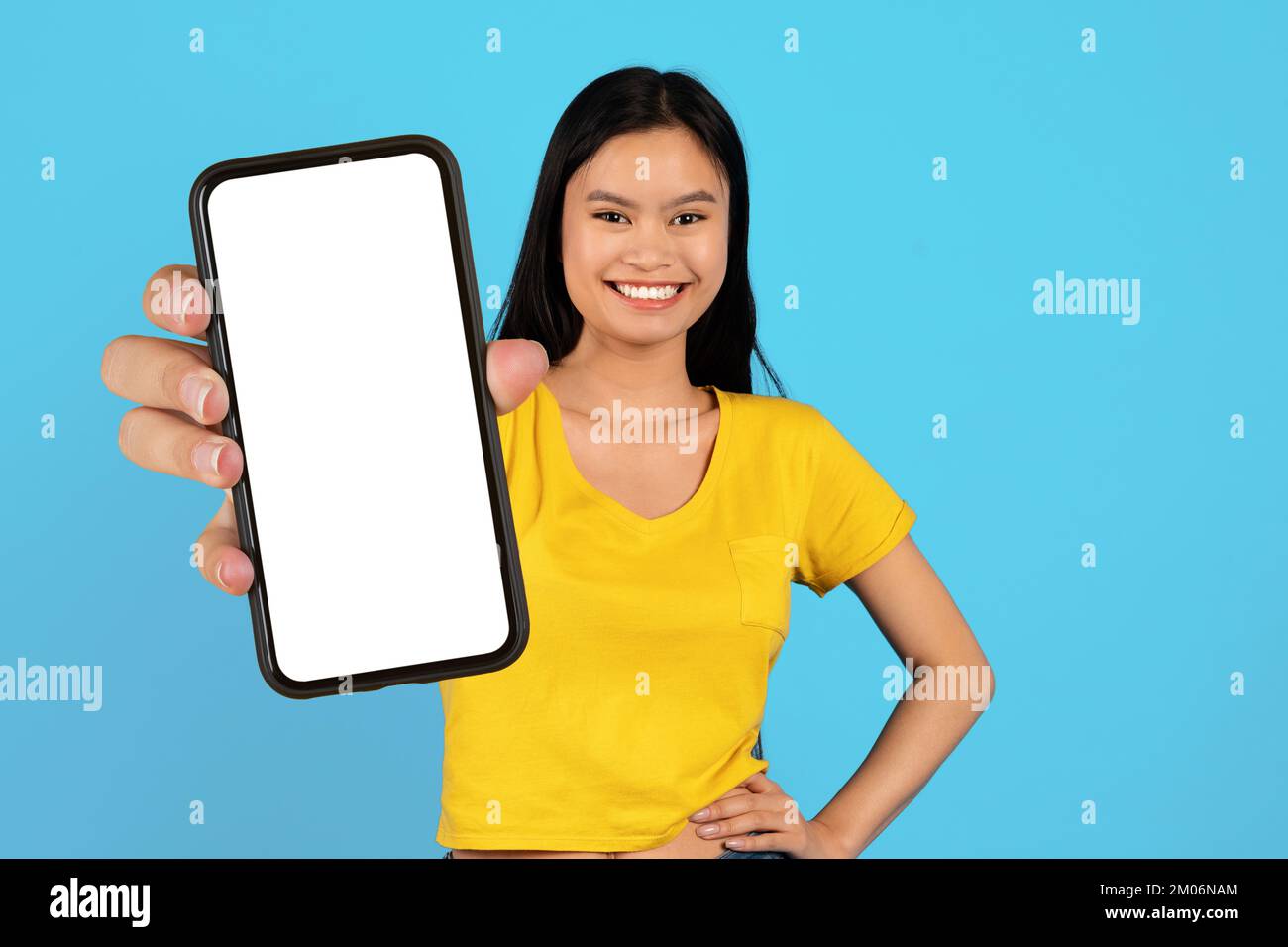 Fröhliche Millenial korean Bloggerin in gelbem T-Shirt zeigt Smartphone mit leerem Bildschirm Stockfoto