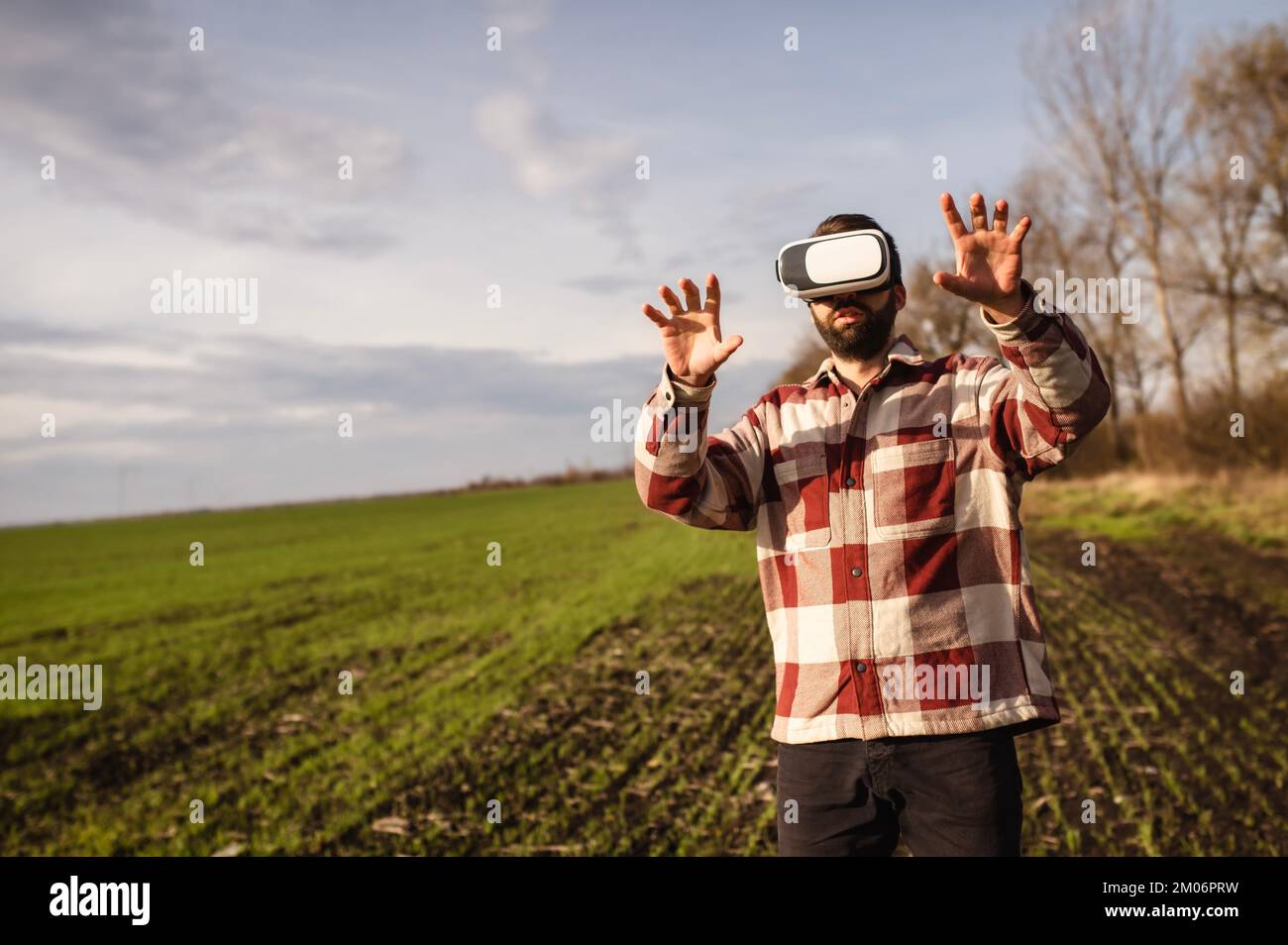 Junger Mann, der bei Sonnenuntergang in einer Virtual-Reality-Brille auf einem Weizenfeld steht Stockfoto