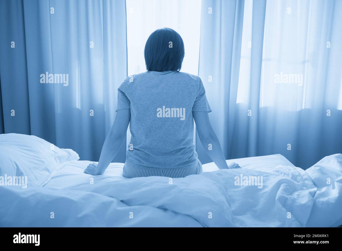 Traurige Frau, die auf dem Bett im einsamen Zimmer sitzt, Blick nach hinten Stockfoto