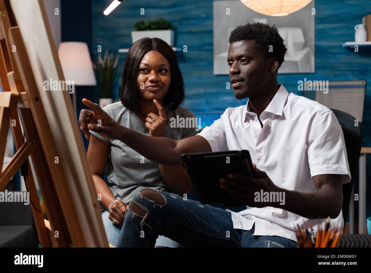 Professionelle Skizzierlehrerin, die Kunsttechniken an männliche Künstler lehrt. Zeichnungsprofessor zur Korrektur von Kunstwerken afroamerikanischer männlicher Schüler in einer Kunstwerkstatt. Stockfoto