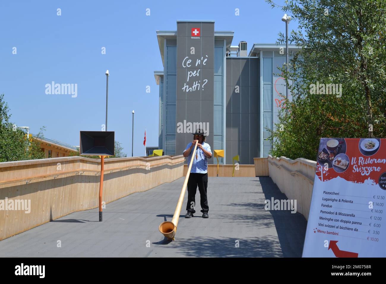 Alphorn-Spieler in seinem traditionellen Kostüm steht und spielt Musik am Eingang des Schweizer Pavillons auf der EXPO Milano 2015 - beste Einladung. Stockfoto