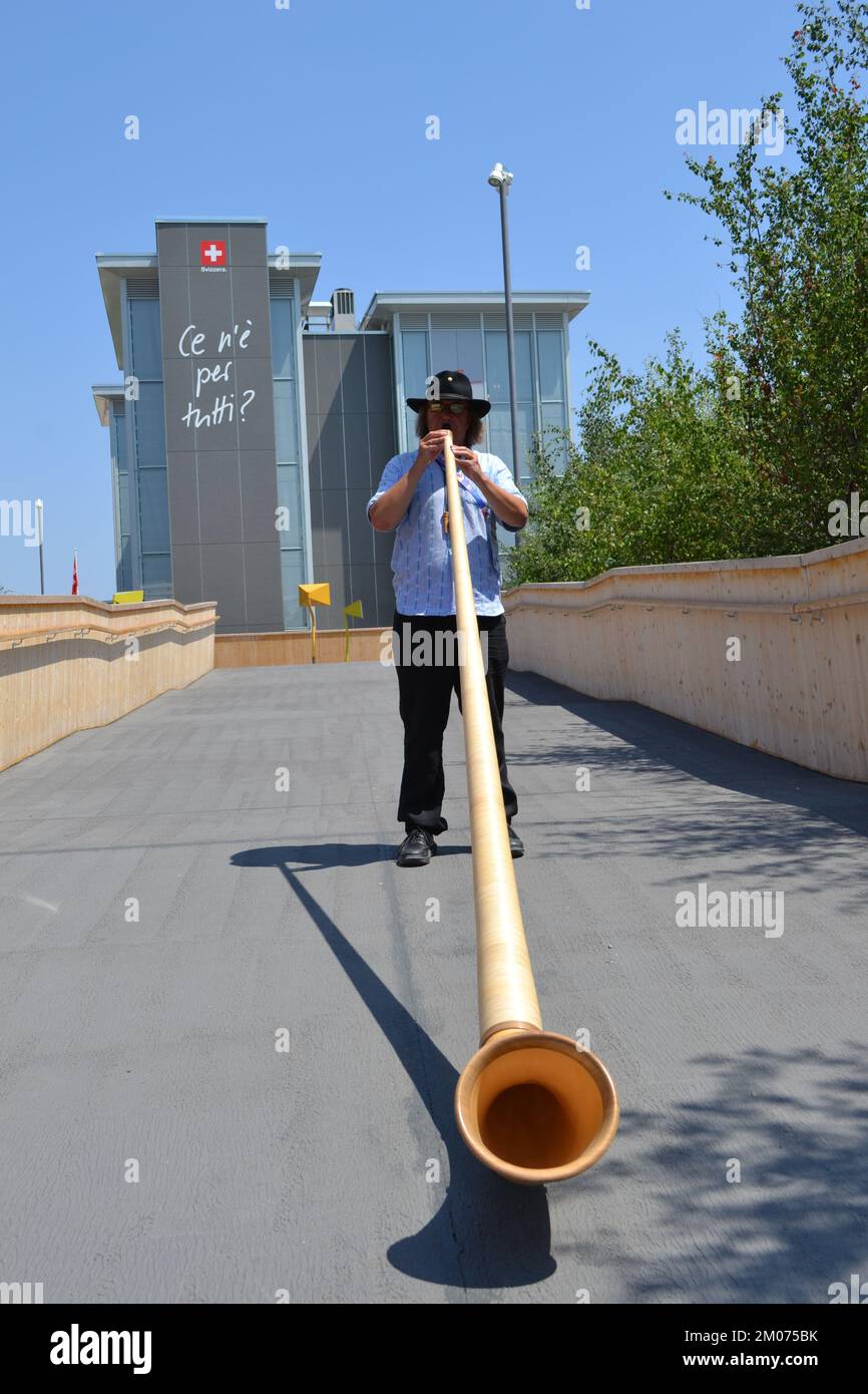 Alphorn-Spieler in seinem traditionellen Kostüm steht und spielt Musik am Eingang des Schweizer Pavillons auf der EXPO Milano 2015 - beste Einladung. Stockfoto