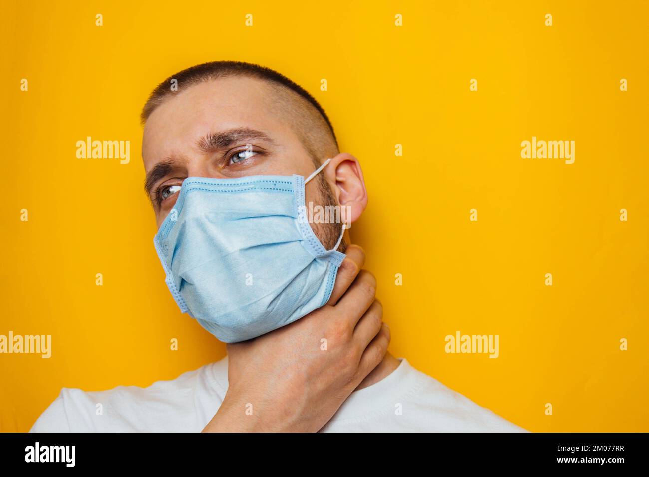 Der Typ hält seine Kehle mit der Hand und zeigt, dass es weh tut. Der maskierte Mann schaut in die Kamera. Erkältungen, Grippe, Virus, Quarantäne, Epidemie Stockfoto