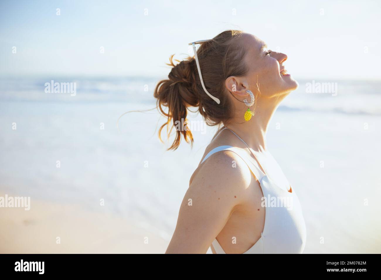 Lächelnde moderne Frau in weißer Strandbekleidung am Strand, entspannend. Stockfoto