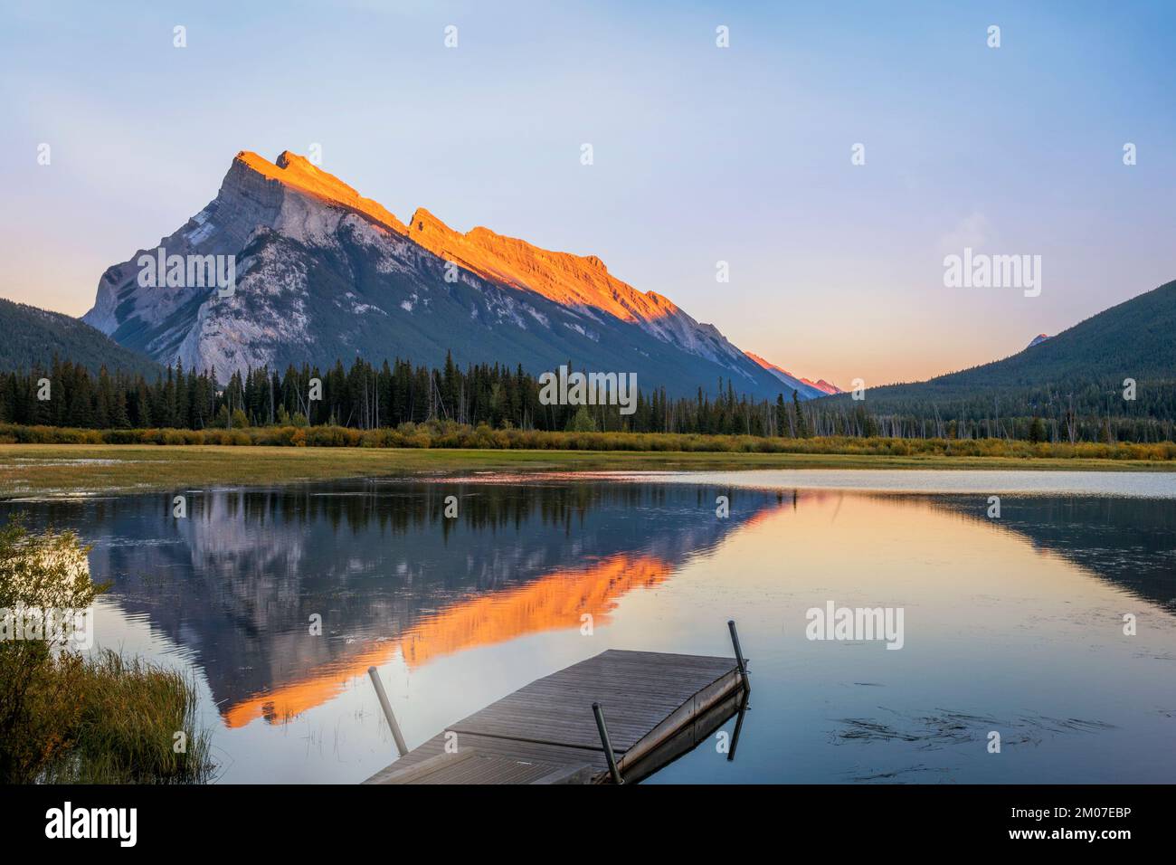 Ein hölzerner Pier erstreckt sich in den zwei Jack Lake im Banff National Park, wobei der Mount Rundle in den Kanadischen Rocky Mountains dramatisch dahinter aufragt. Stockfoto