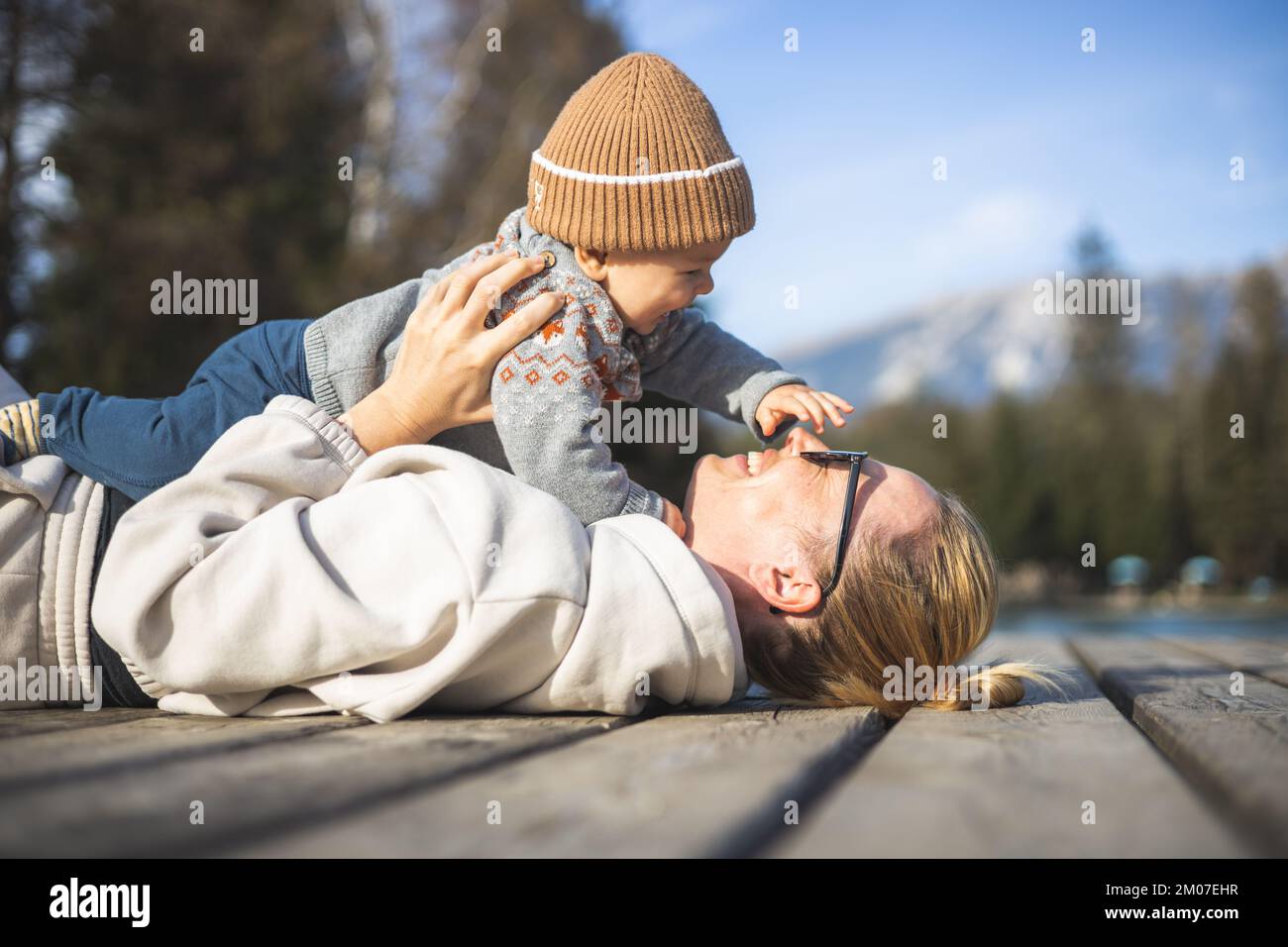 Glückliche Familie. Junge Mutter, die mit ihrem kleinen Jungen an einem sonnigen Herbsttag außerhalb der Tür spielt. Porträt von mutter und Sohn auf einer hölzernen Plattform am See. Positive menschliche Emotionen, Gefühle, Freude Stockfoto