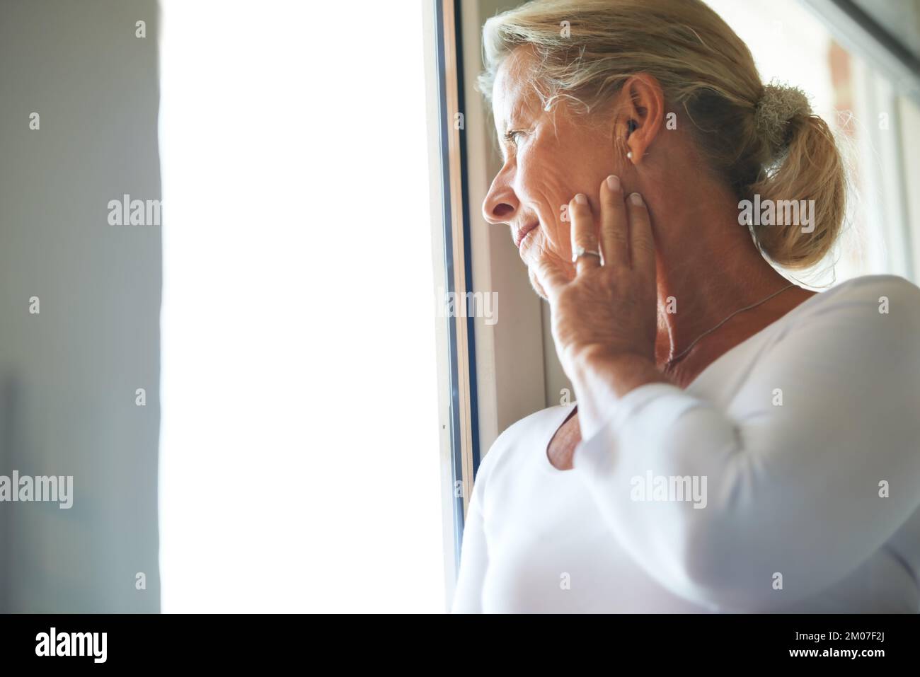 Verloren in ihren Gedanken. Eine rücksichtsvolle Seniorin, die aus dem Fenster schaut. Stockfoto