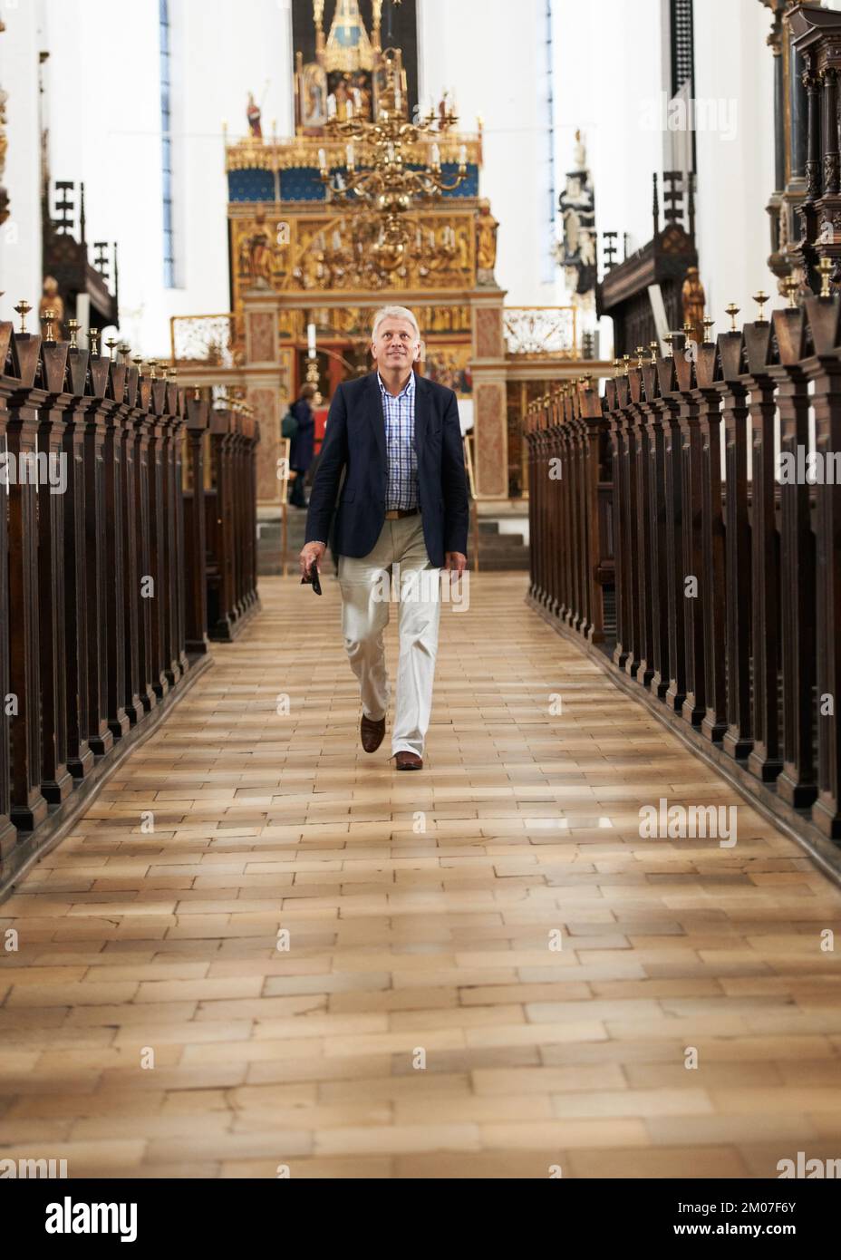 Im Haus der Götter. Porträt eines Seniorenmannes, der den Gang einer Kirche entlang geht. Stockfoto