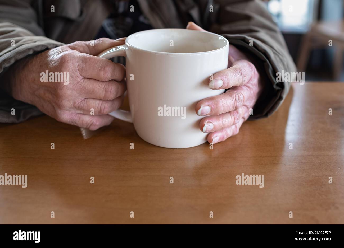 Eine alte Frau hält eine Tasse heißes Kaffeegetränk in den Händen. Nahaufnahme der Hand einer älteren Frau, die eine Tasse Tee oder Kaffee hält. Kopieren Sie den Text, und wählen Sie aus Stockfoto