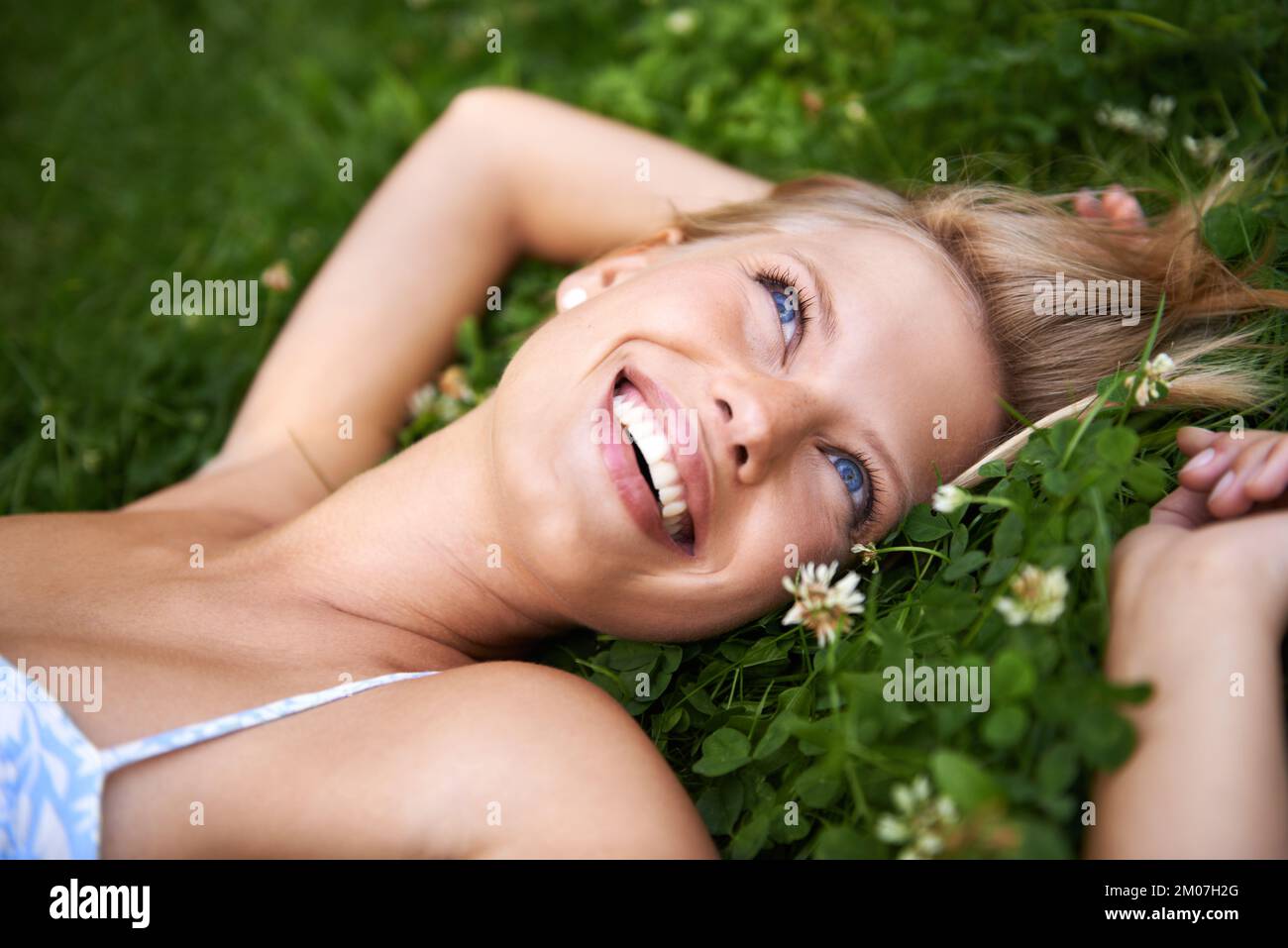 Sommertagsträume. Hübsche, junge blonde Frau, die auf dem Gras lag, während sie aufblickte und lächelte. Stockfoto