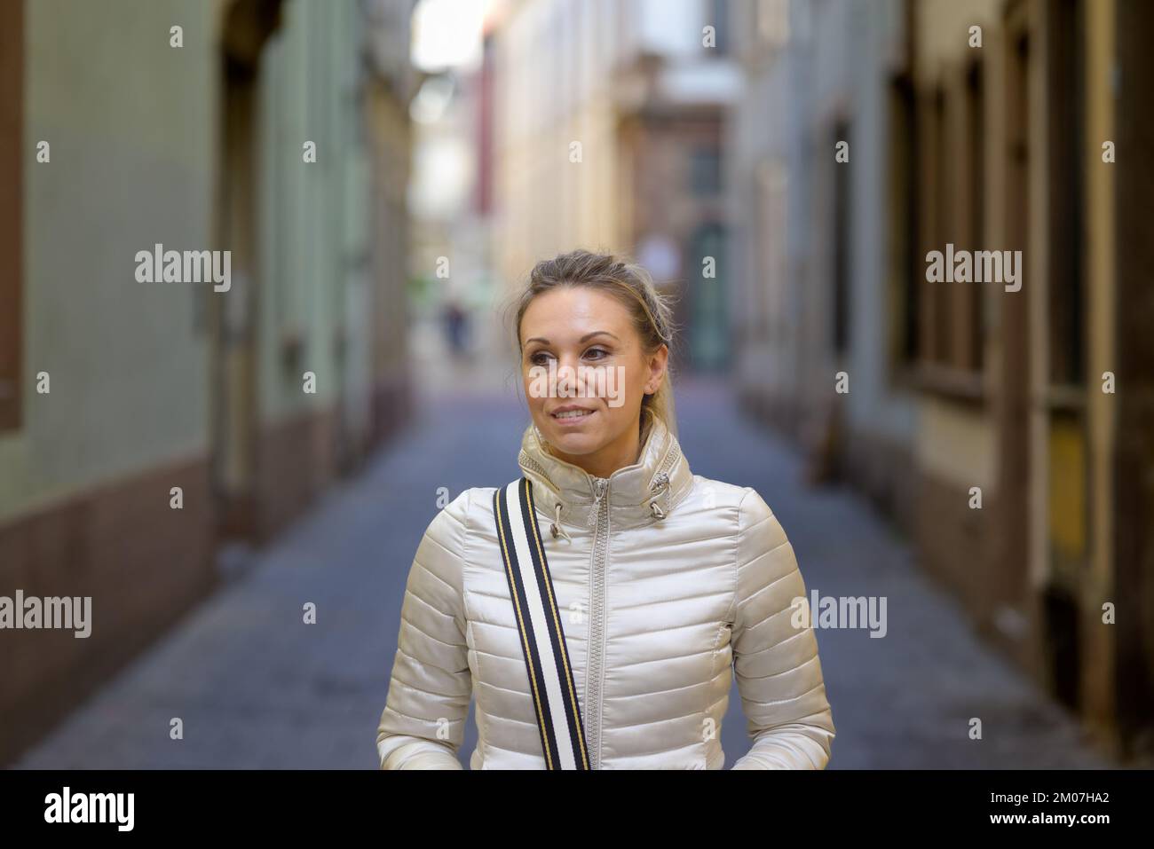 Eine attraktive Frau mittleren Alters mit blonden Haaren und einem Pferdeschwanz, die eine metallische Jacke trägt und eine Handtasche über der Schulter trägt, geht nach unten Stockfoto