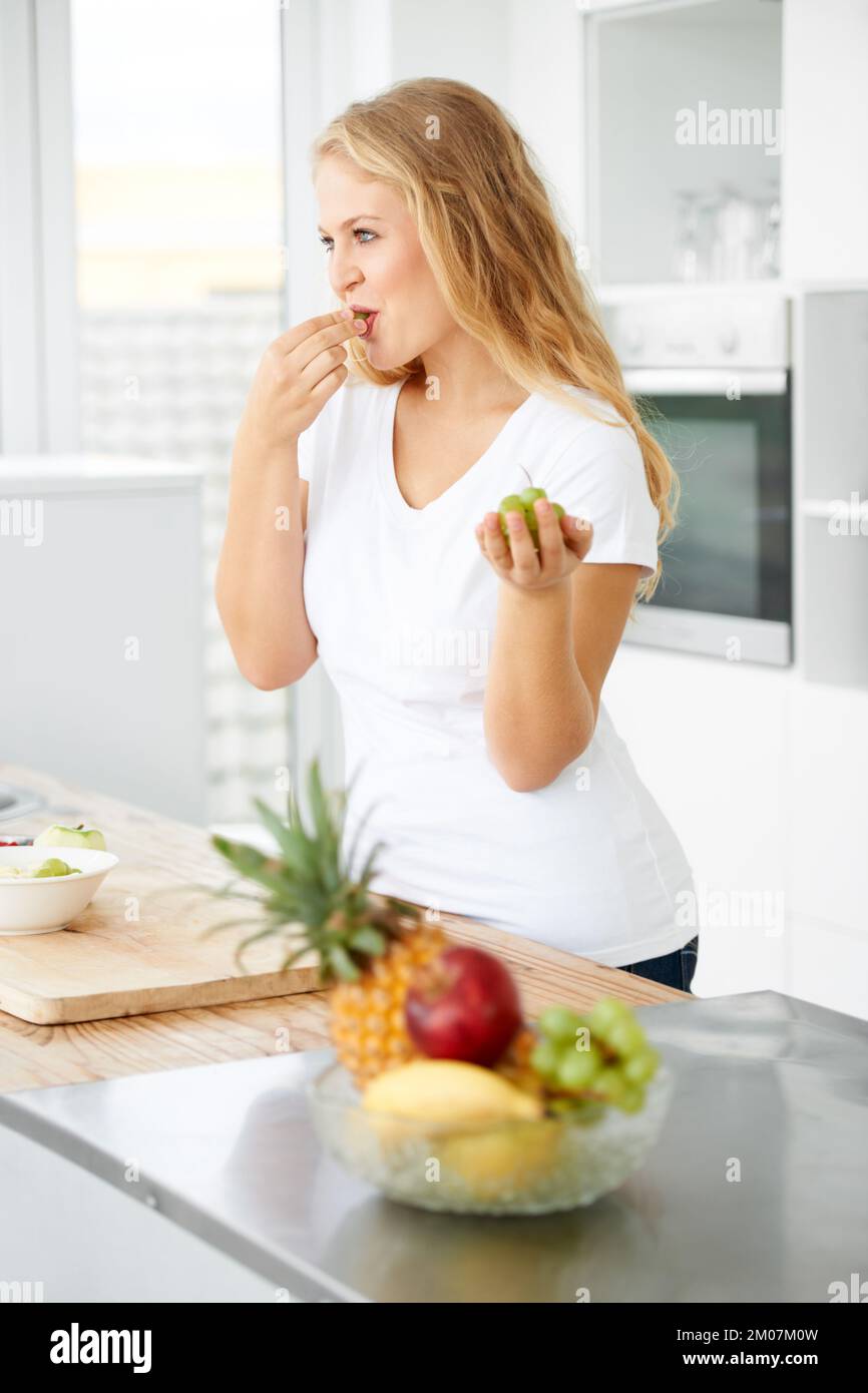 Hmmmmmm so frisch. Kurvige junge Frau, die Trauben in ihrer Küche isst. Stockfoto
