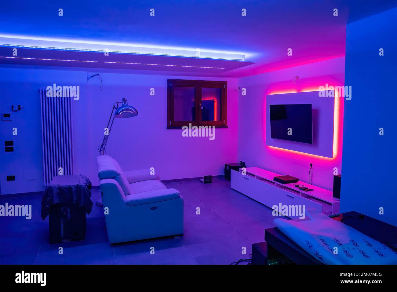 Ich ziehe in ein neues Haus. Innenraum des Hauses. Ideen für das Wohnzimmer im Keller. Unterhaltungsraum mit Fernseher und LED-Farbstreifen. Stockfoto