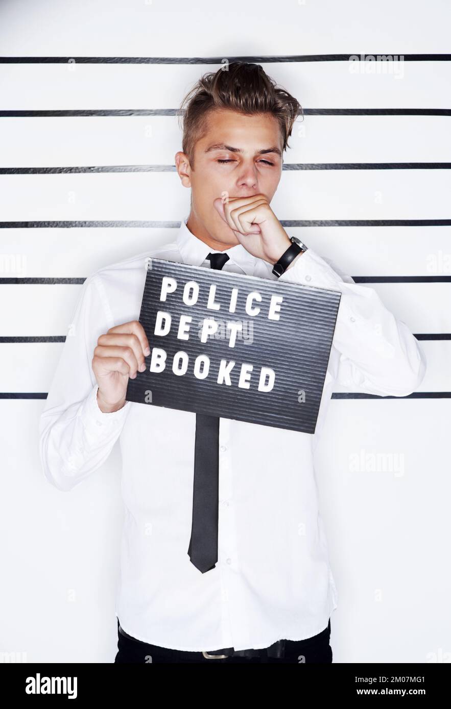 Erwischt. Verbrecherfoto eines jungen Mannes mit Hemd und Krawatte, der ein Polizeischild hochhält. Stockfoto
