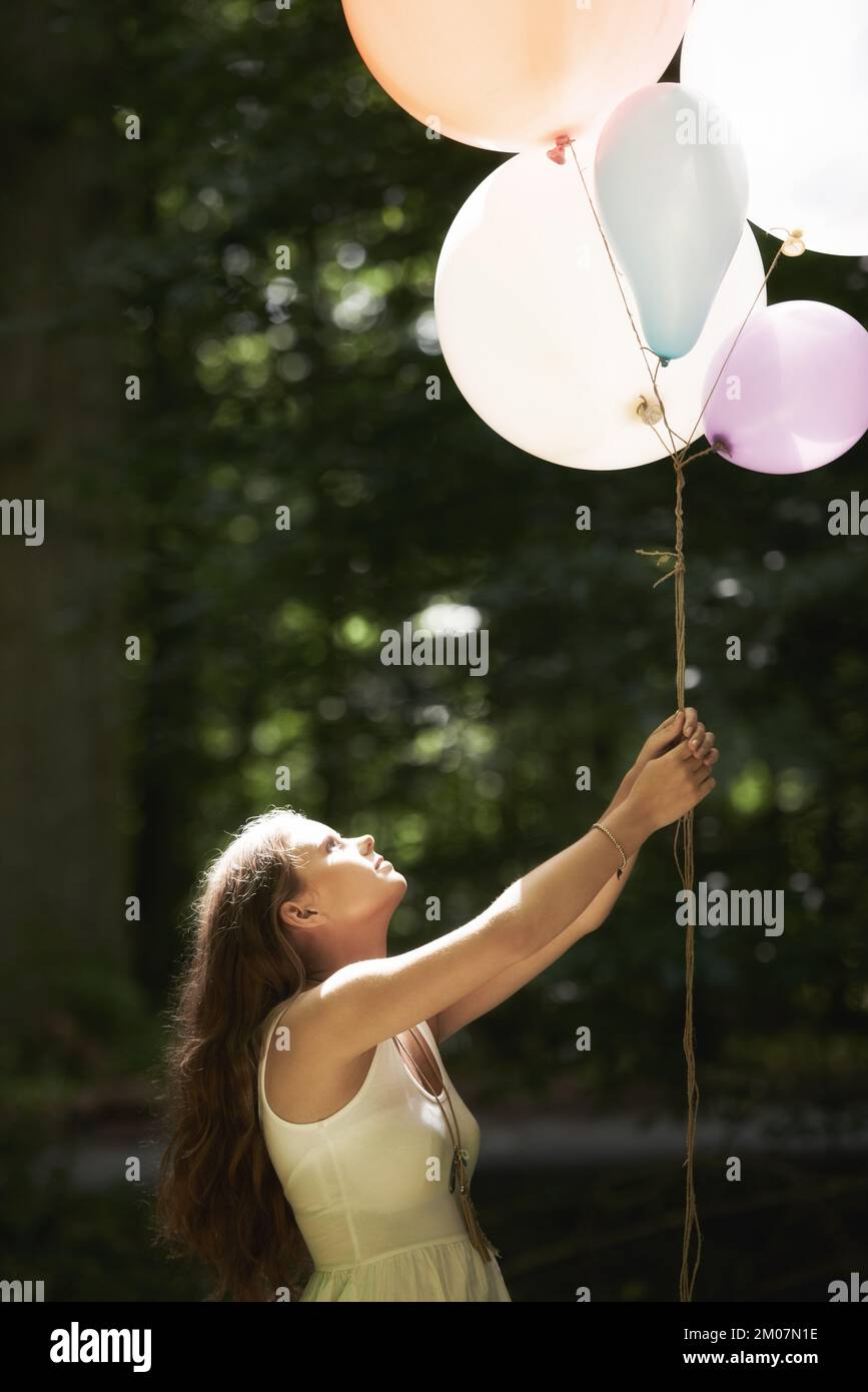 Eine hübsche junge Frau, die einen Haufen Ballons im Wald hält Stockfoto