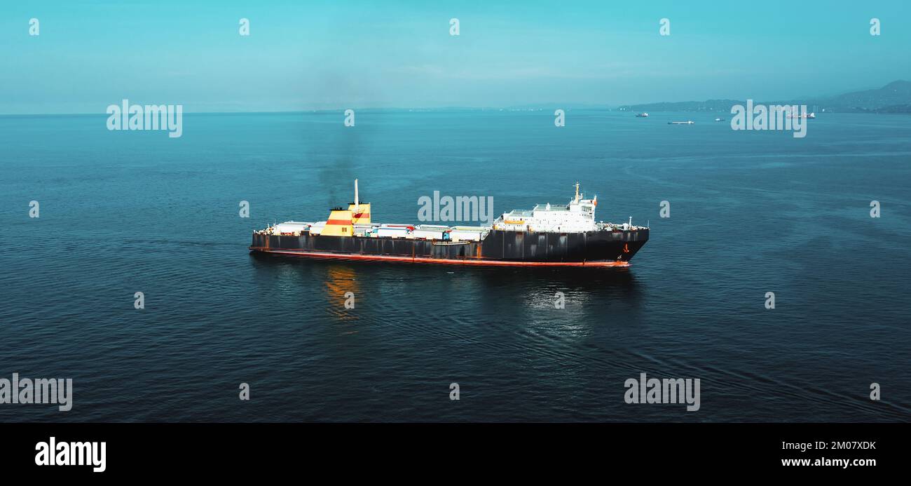 Frachtschiff mit LKWs und Containern auf See, Luftaufnahme von der Drohne. Kommerzielle Handelslogistik und internationales Transportkonzept. Stockfoto