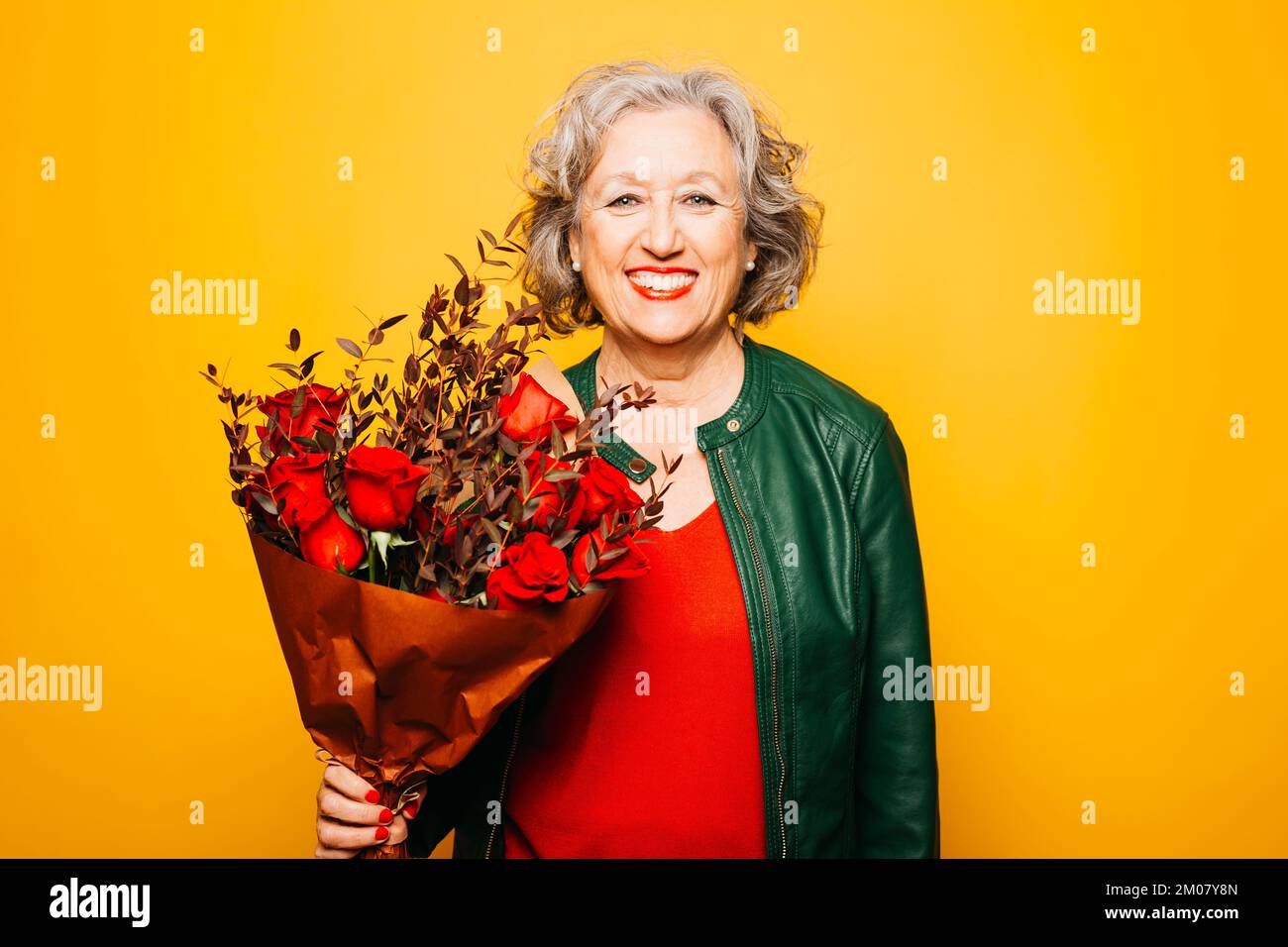 Porträt einer Seniorin mit rotem Rosenstrauß auf gelbem Hintergrund Stockfoto