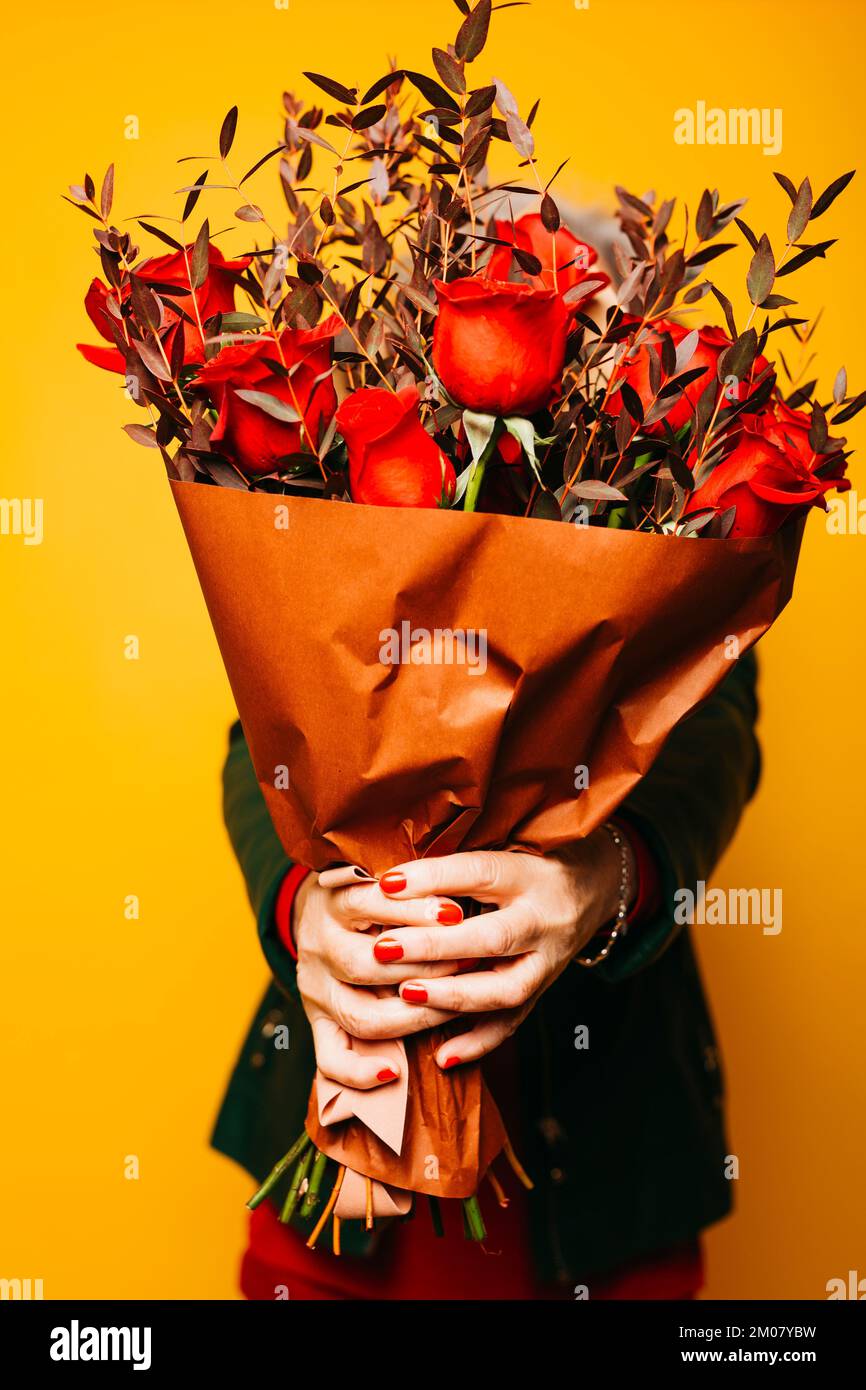 Roter Rosenstrauß, der von einer älteren Frau auf gelbem Hintergrund gehalten wird Stockfoto