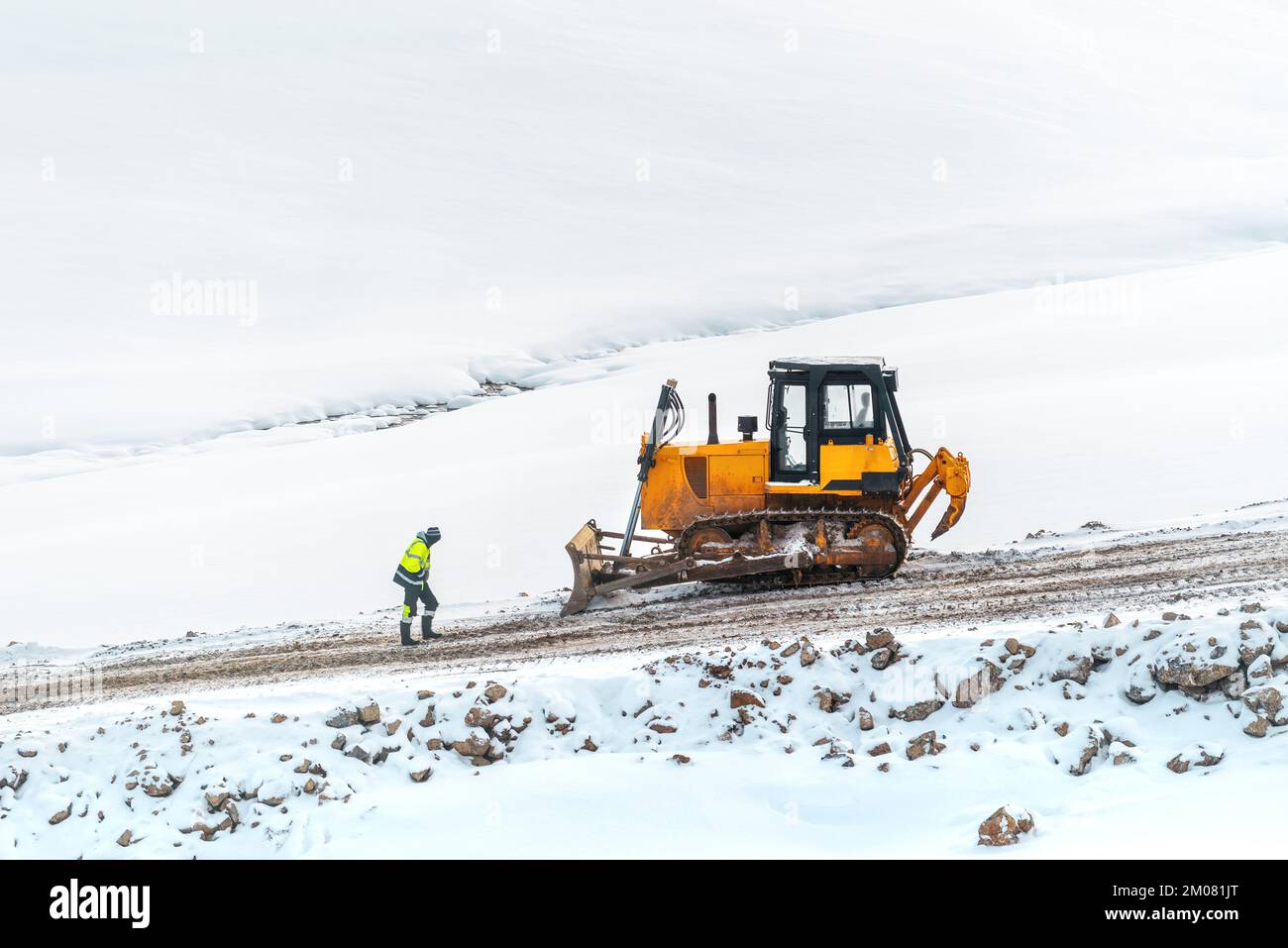 Industriearbeiter vor einem schweren Bulldozer auf einer Straßenbaustelle im Winter Stockfoto