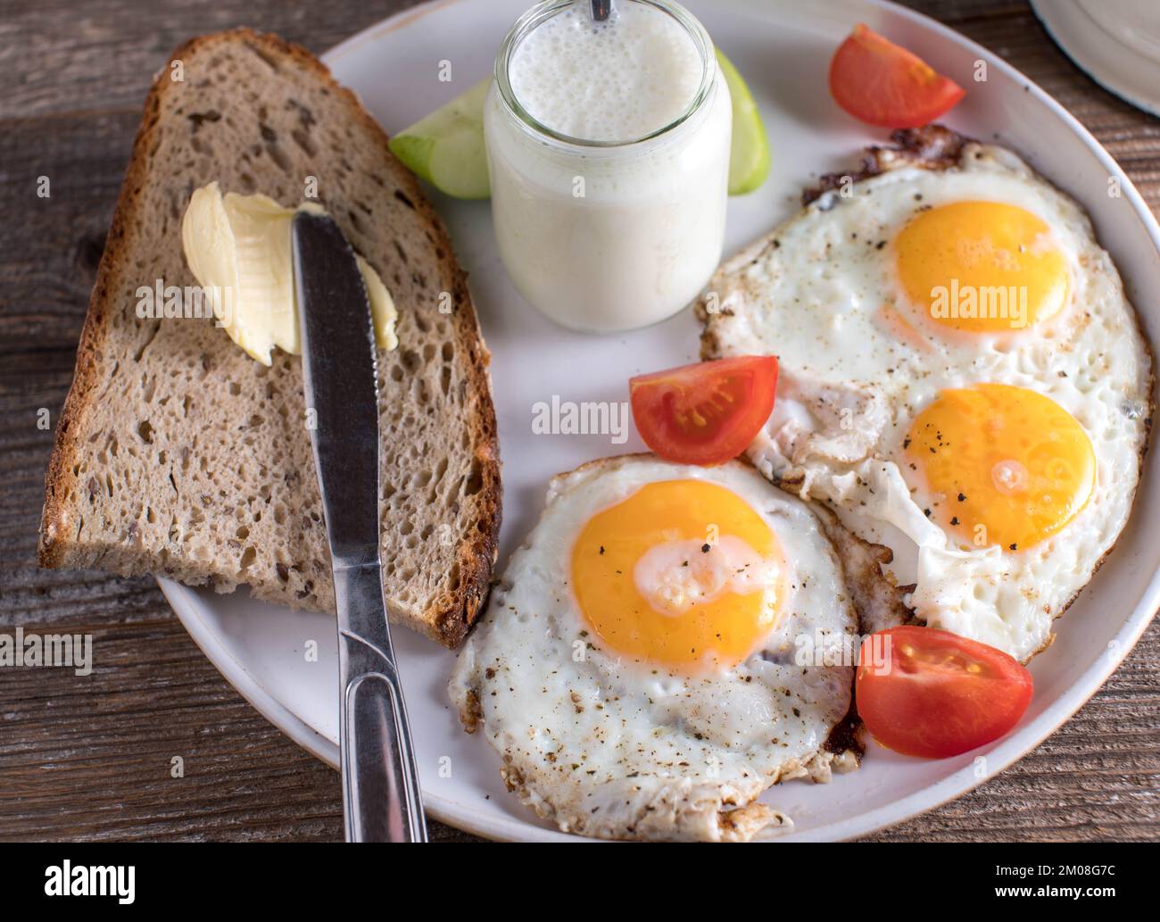 Frühstücksteller mit Roggenbrot, Butter, hausgemachtem Apfeljoghurt und Spiegeleiern, sonnige Seite nach oben auf einem Holztisch. Nahaufnahme und Draufsicht Stockfoto