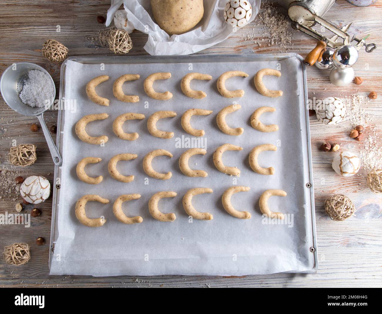 Vanillekipferl oder Vanillesoncent roh und ungebacken auf einem Backblech mit Teig und Küchenutensilien und weihnachtsdekoration. Flach verlegt Stockfoto