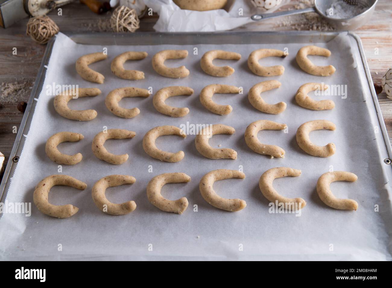 Deutsche weihnachtskekse, Vanillekipferl oder Vanillesrescent roh und ungebacken auf einem Backblech mit Küchenutensilien und Dekoration Stockfoto