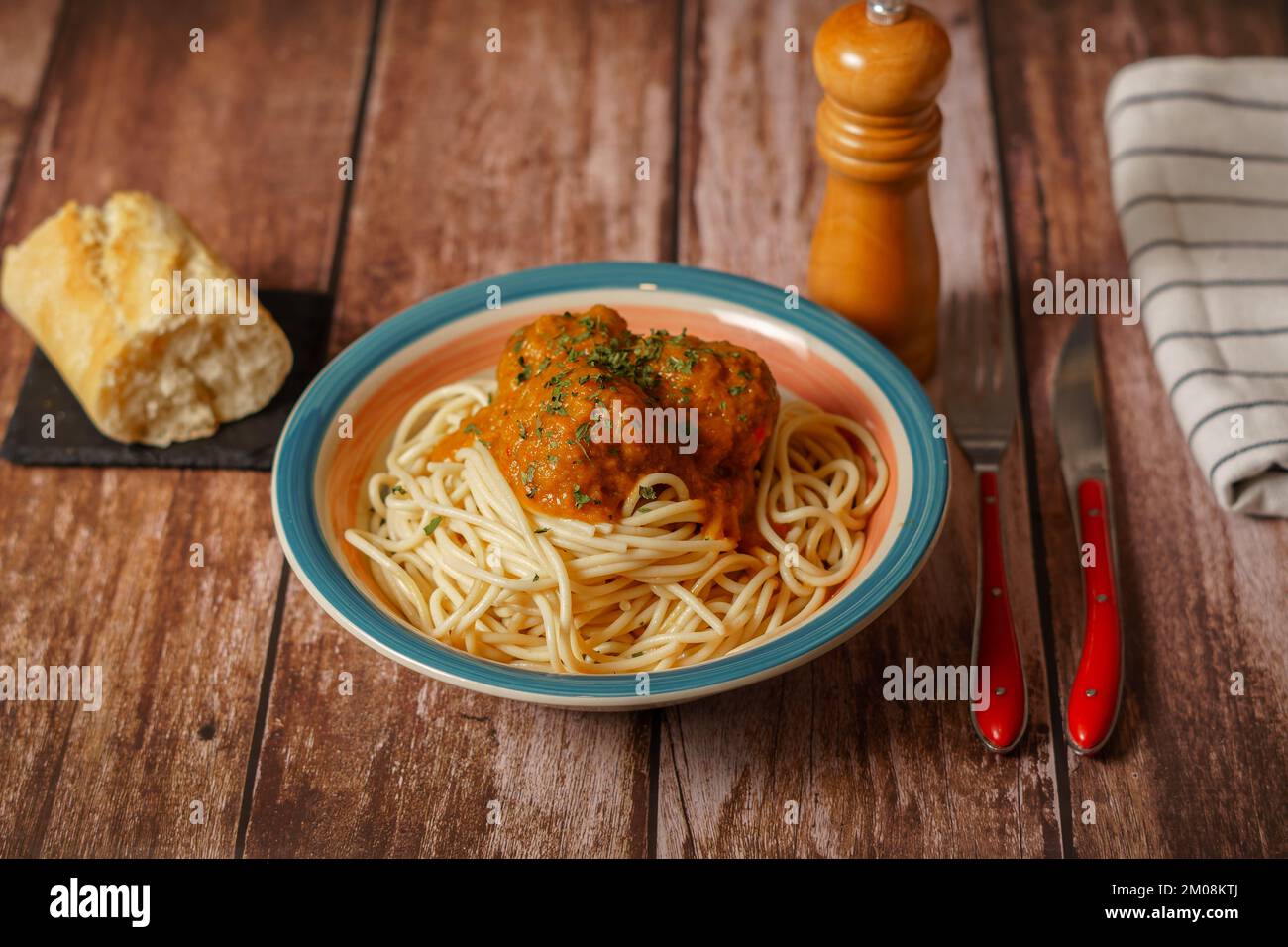Teller mit Fleischbällchen mit Spaghetti mit Besteck und Brot- und Pfefferstreuer auf einem Holztisch Stockfoto