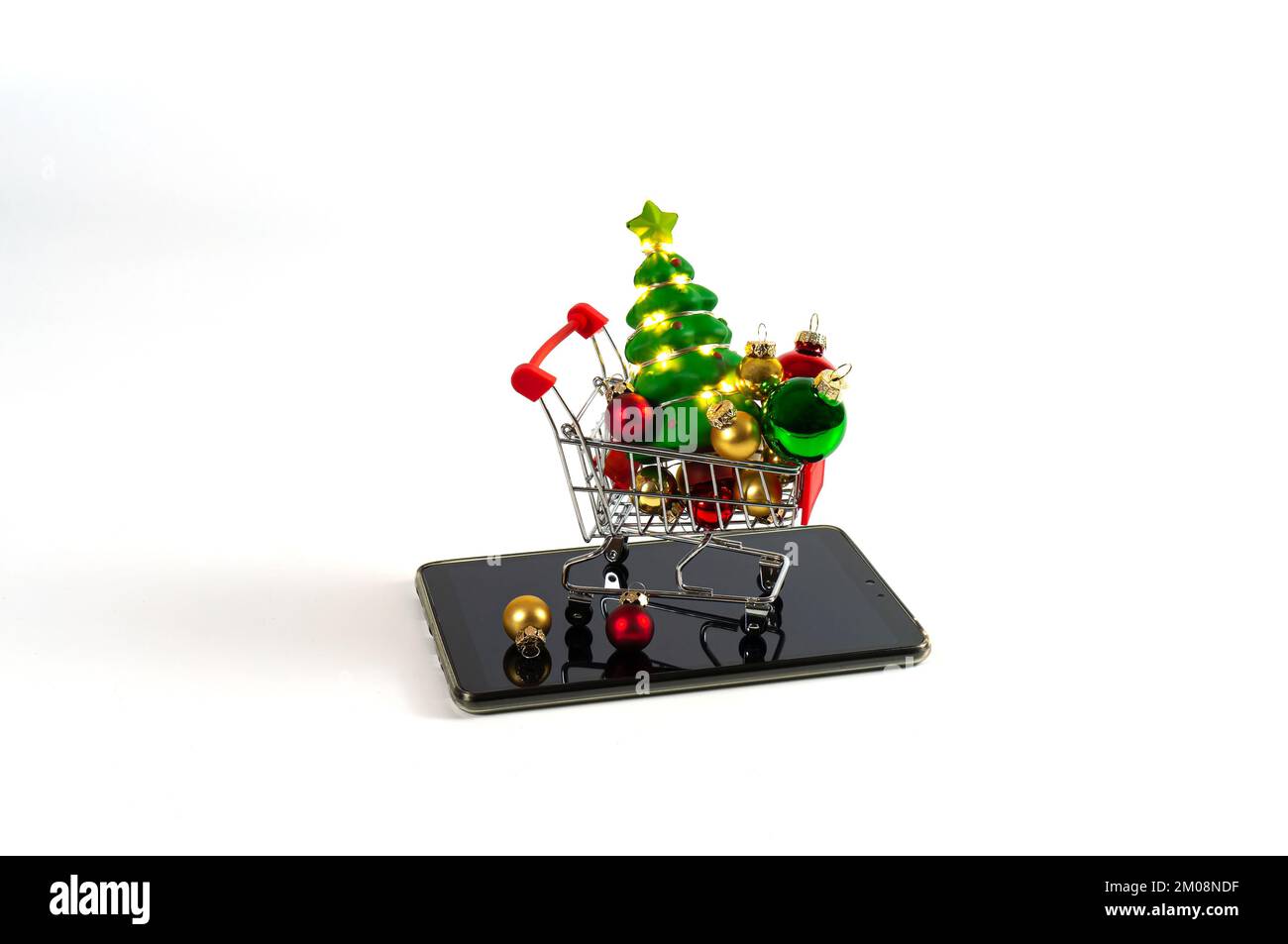 Einkaufswagen mit weihnachtsbällen und Baum mit Girlanden auf dem Tablet. Einfacher Hintergrund. Stockfoto