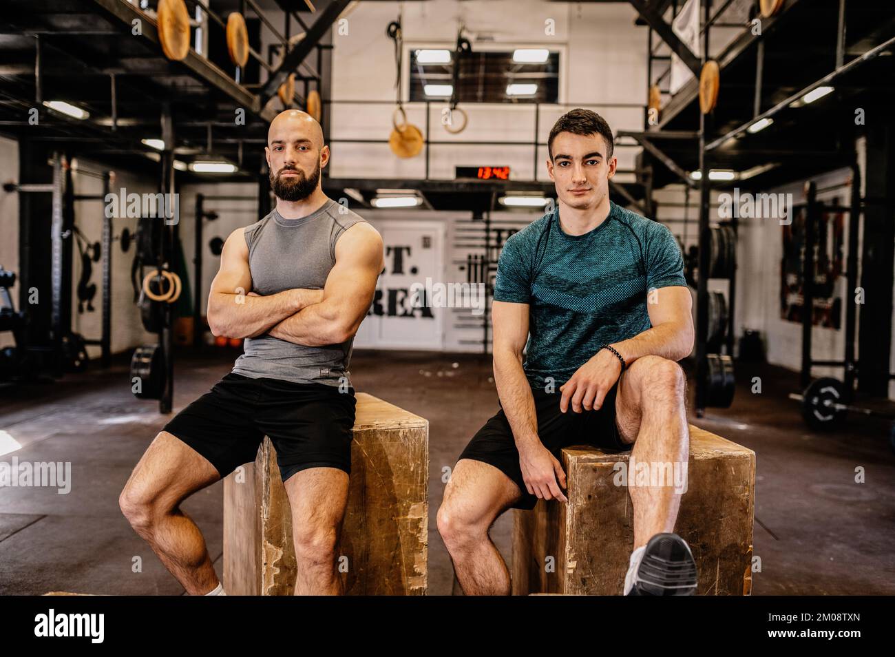 Zwei Männer sitzen auf Holzkisten und schauen in die Kamera. Nach einem harten Workout ausruhen. Stockfoto