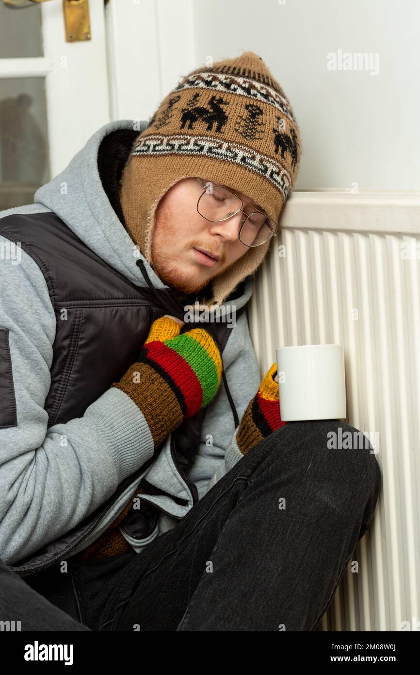 Ein junger Mann, eingewickelt in schweren Mantel, Handschuhe und Hut, der sich mit einer heißen Tasse Tee aufwärmt Stockfoto