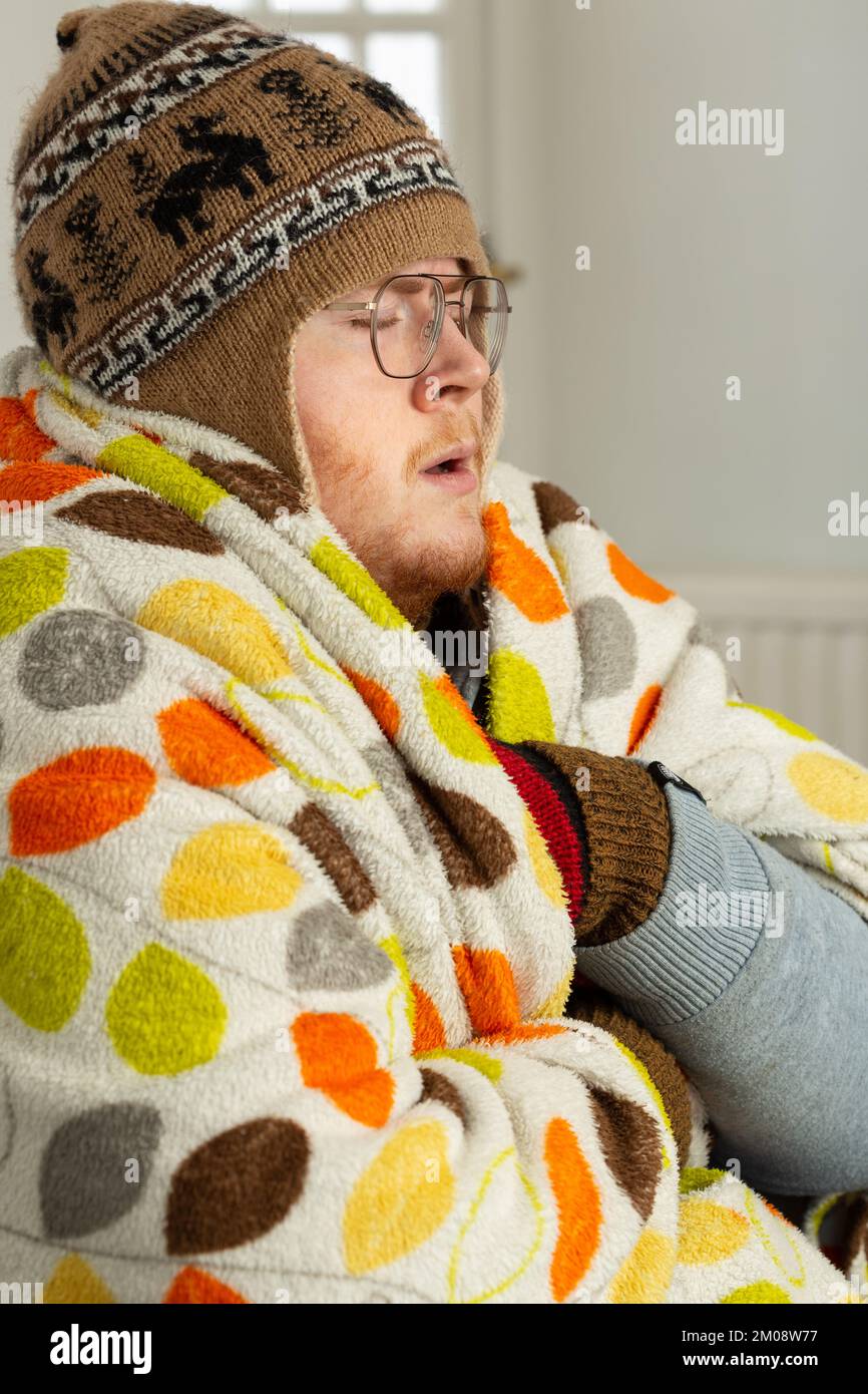 Ein junger Mann, eingewickelt in eine Decke und mit einem Wollmütze drinnen Stockfoto