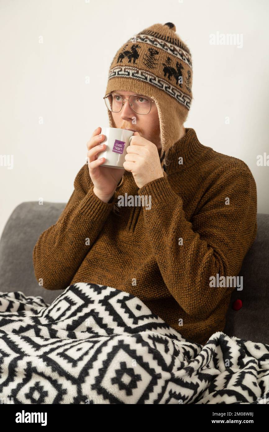Ein junger Mann mit Wollmütze und Pullover, der einen Kräutertee trinkt Stockfoto