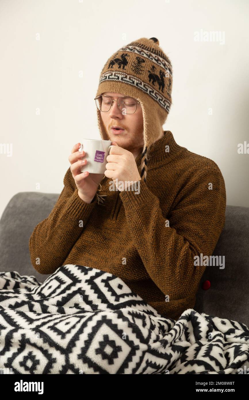 Ein junger Mann mit Wollmütze und Pullover, der einen Kräutertee trinkt Stockfoto