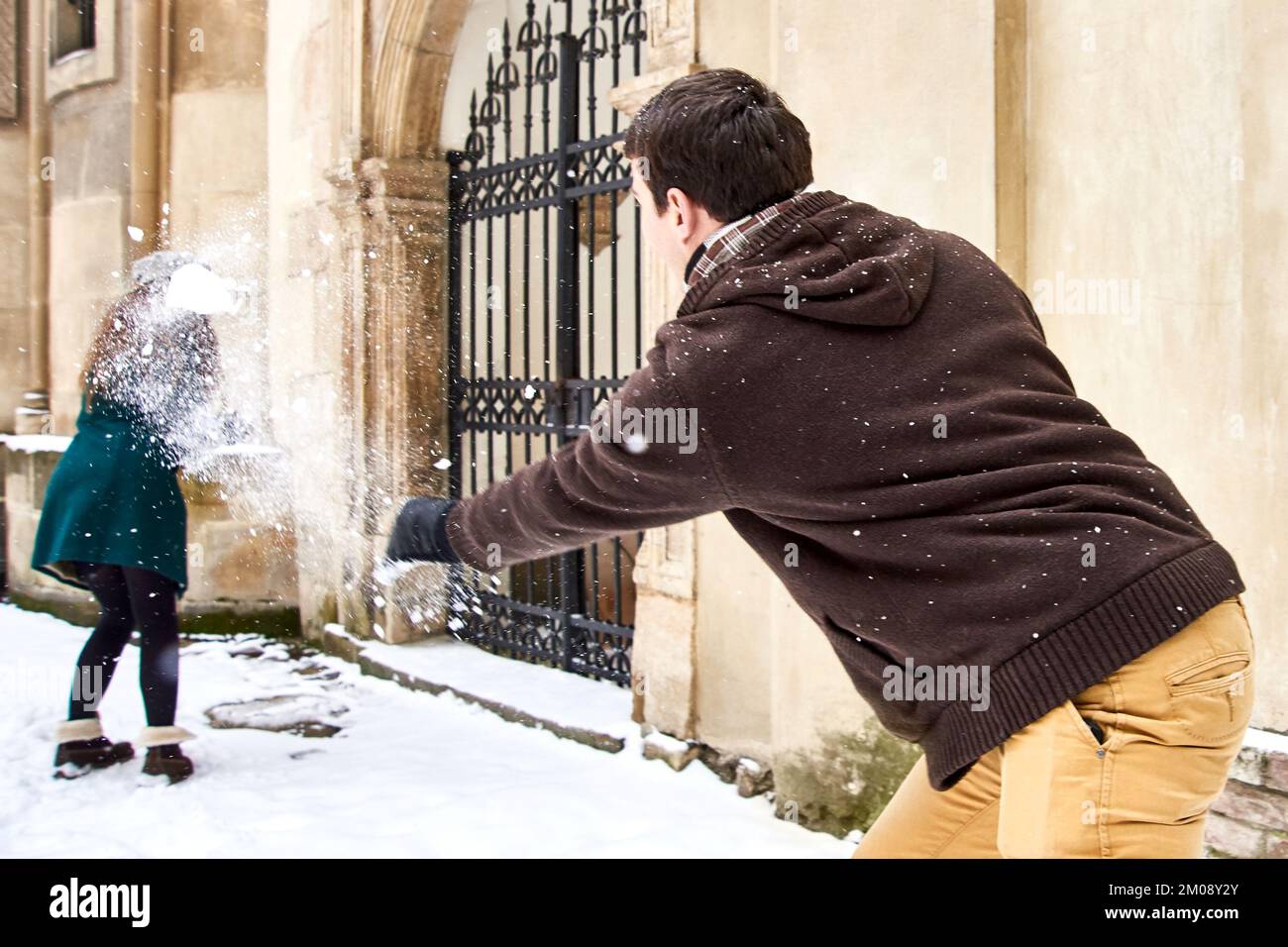 Der Junge wirft Schneeball in einem Mädchen im Garten. Winterspaß und Unterhaltung im Freien Stockfoto