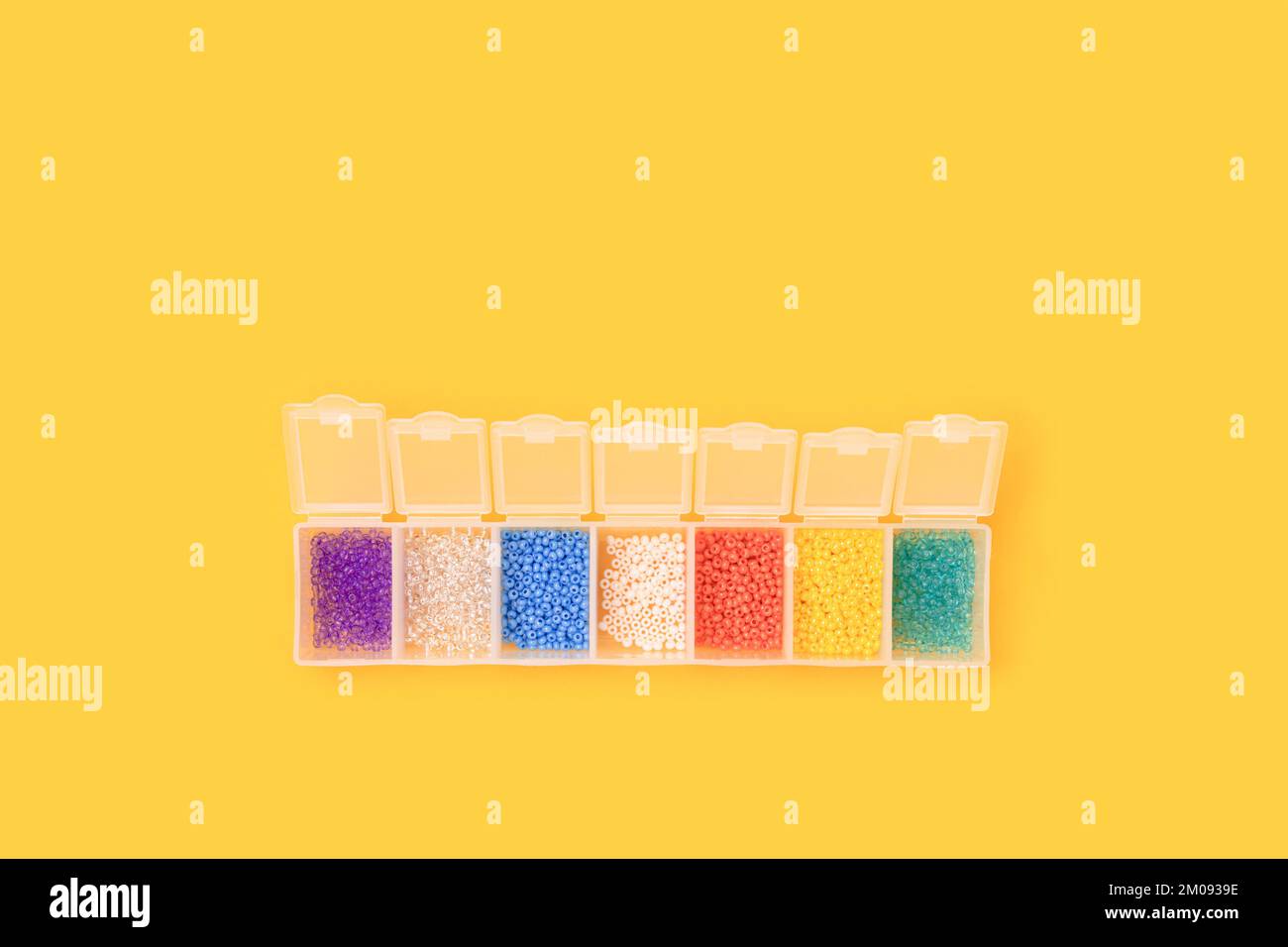 Mehrfarbige Perlen in einem transparenten Aufbewahrungsbehälter auf gelbem Hintergrund. Stockfoto