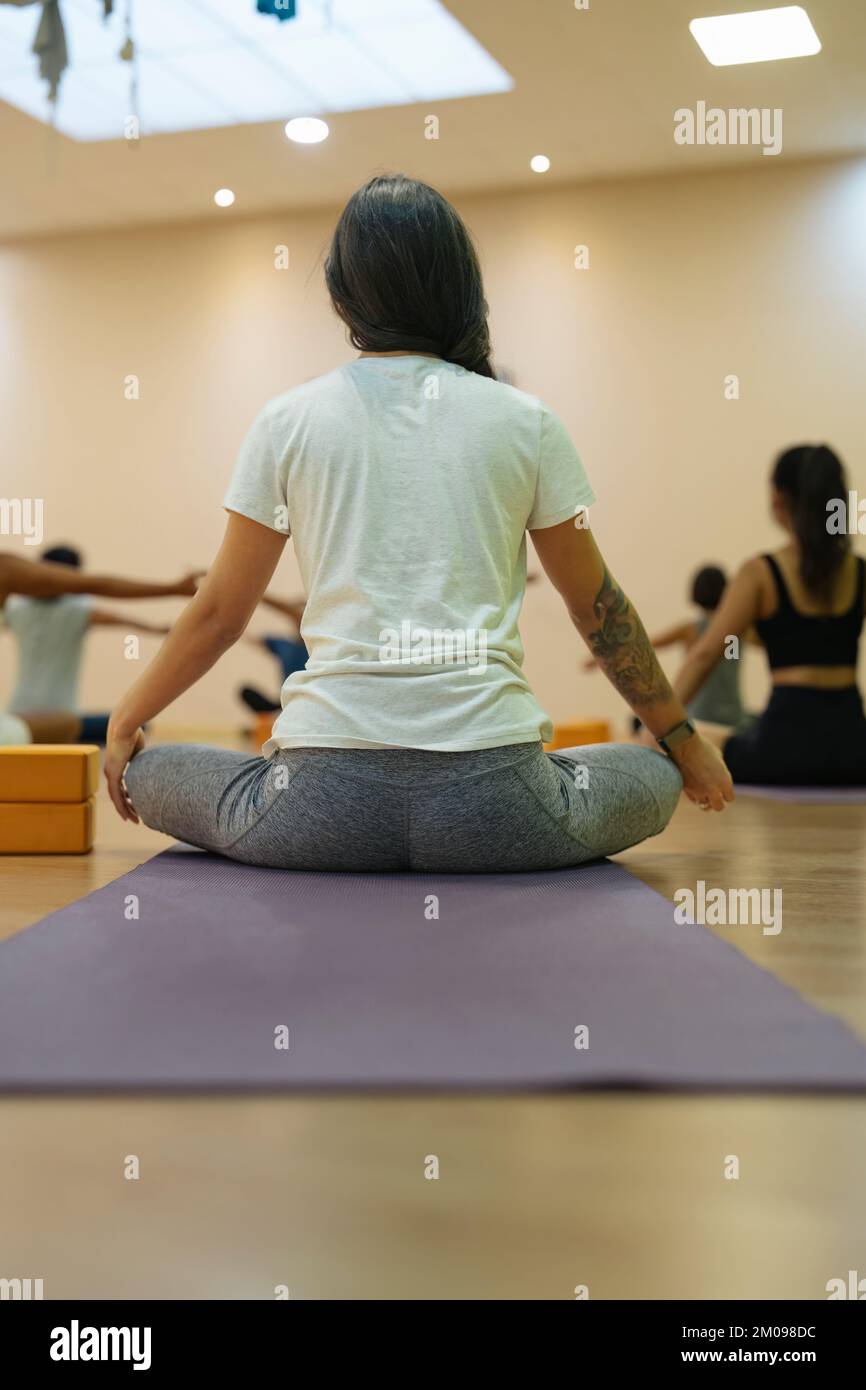 Vertikales Foto einer brünetten Frau, die Yoga in einer Sukhasana-Pose macht Stockfoto