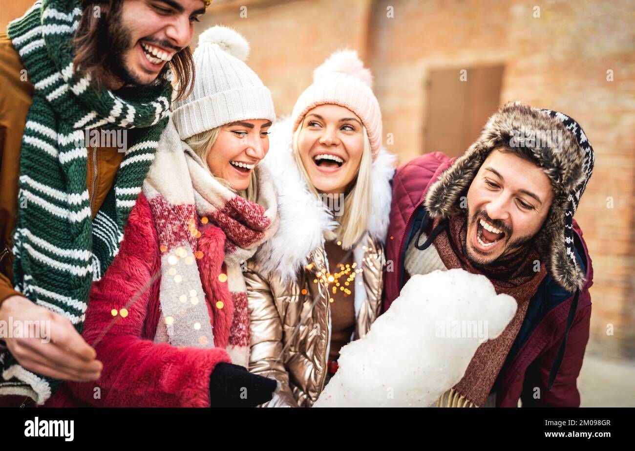 Glückliche Freunde, die auf dem Weihnachtsmarkt im kalten Winter Zuckerwatte essen - Vintage-Urlaubskonzept mit jungen Leuten, die zusammen abhängen Stockfoto